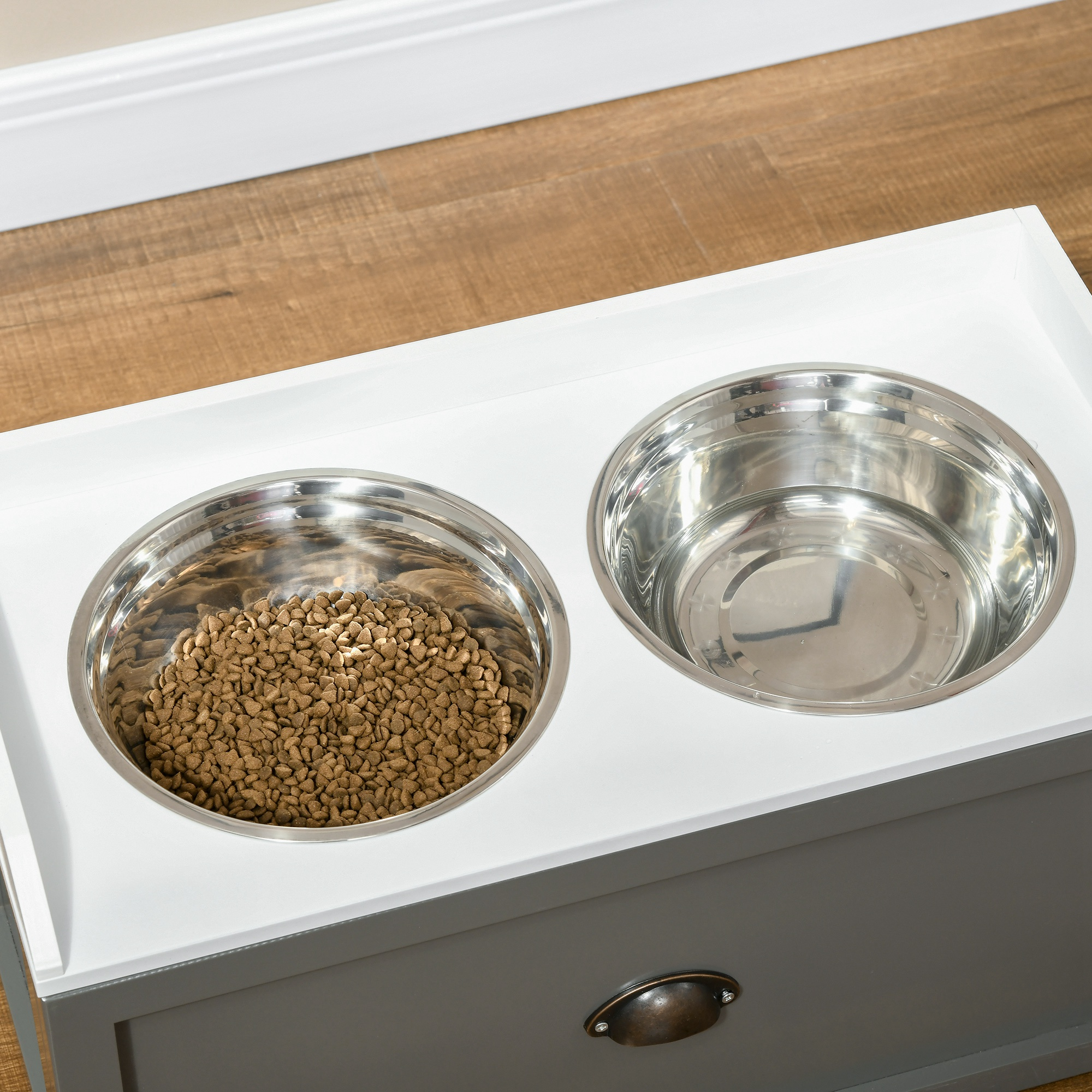 Gabinete blanco con dos cuencos plateados para perros, uno lleno de comida, el otro vacío.
