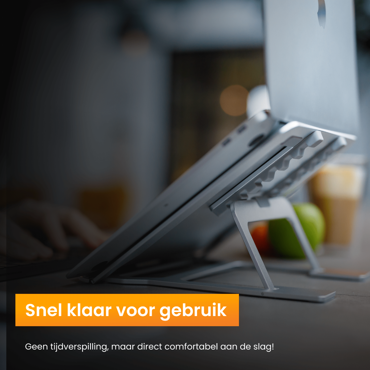 Laptop op een zilveren standaard op een bureau. Handen van een persoon zijn zichtbaar en een groene appel.