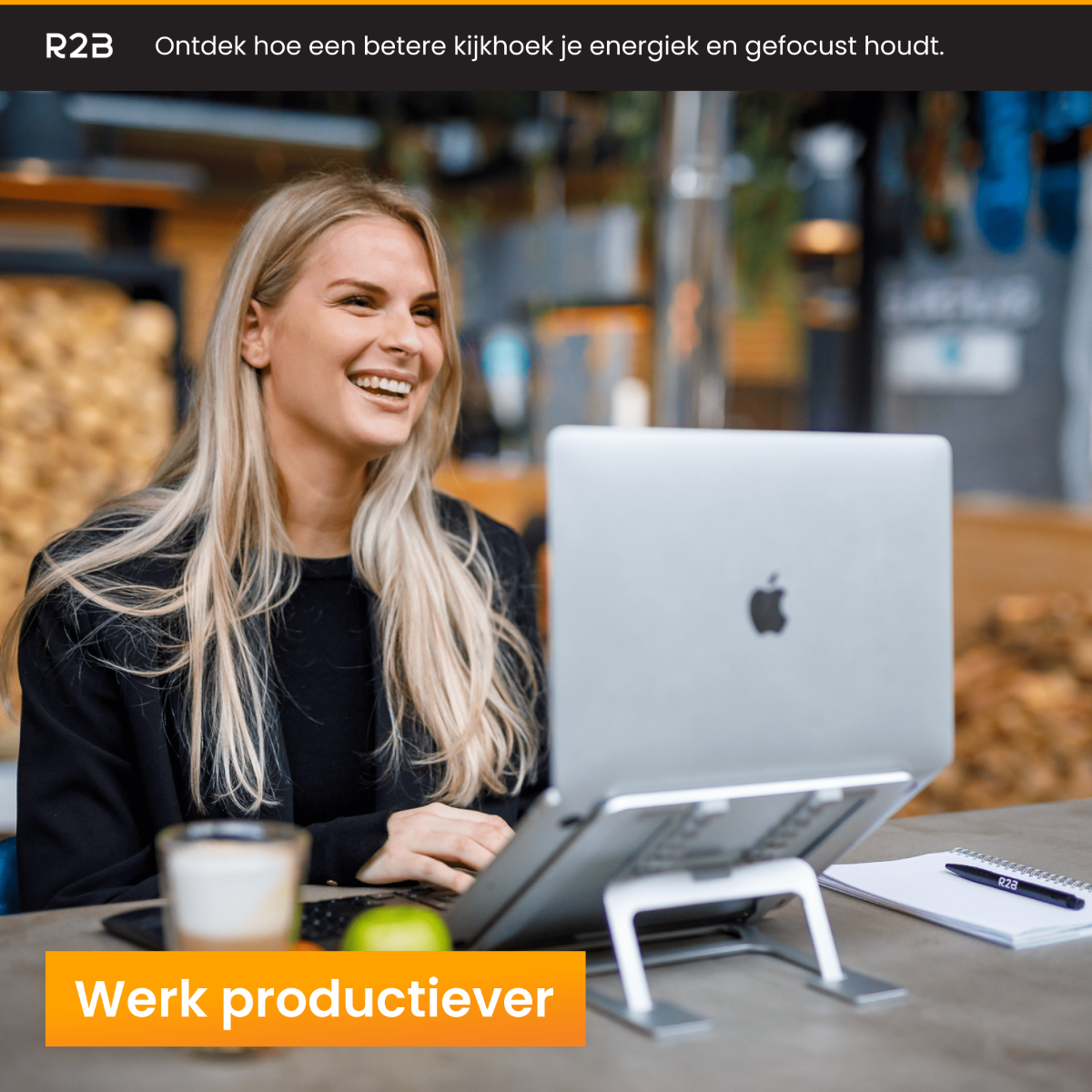 Blonde vrouw lachend, laptop op standaard, met koffie en notitieboekje.