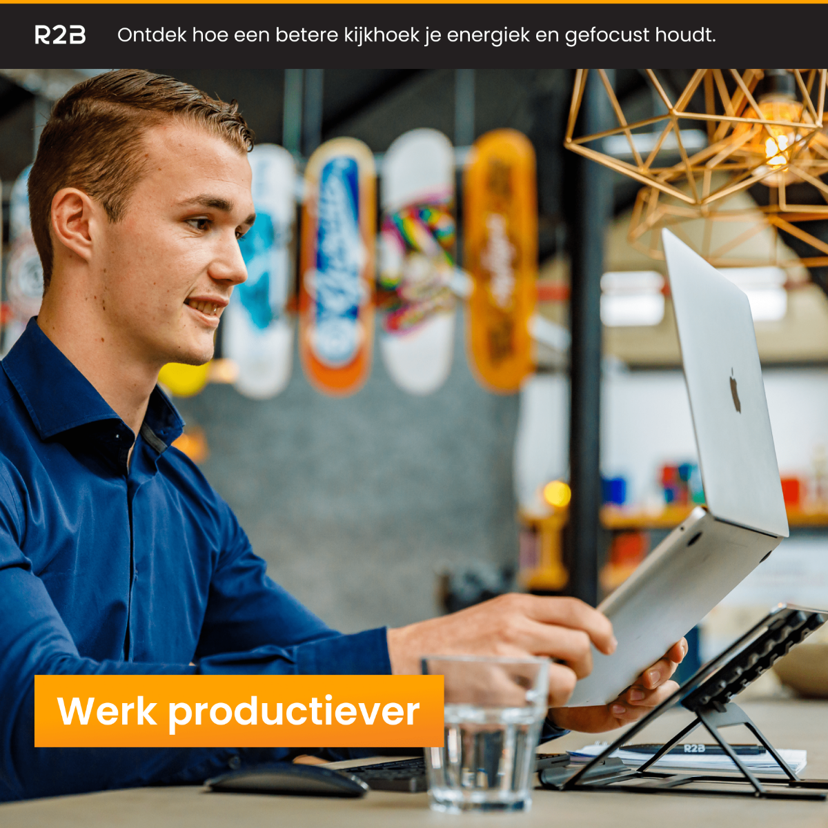 Man die op een laptop werkt aan een bureau. Laptop op een standaard. Glas water. Vage achtergrond.