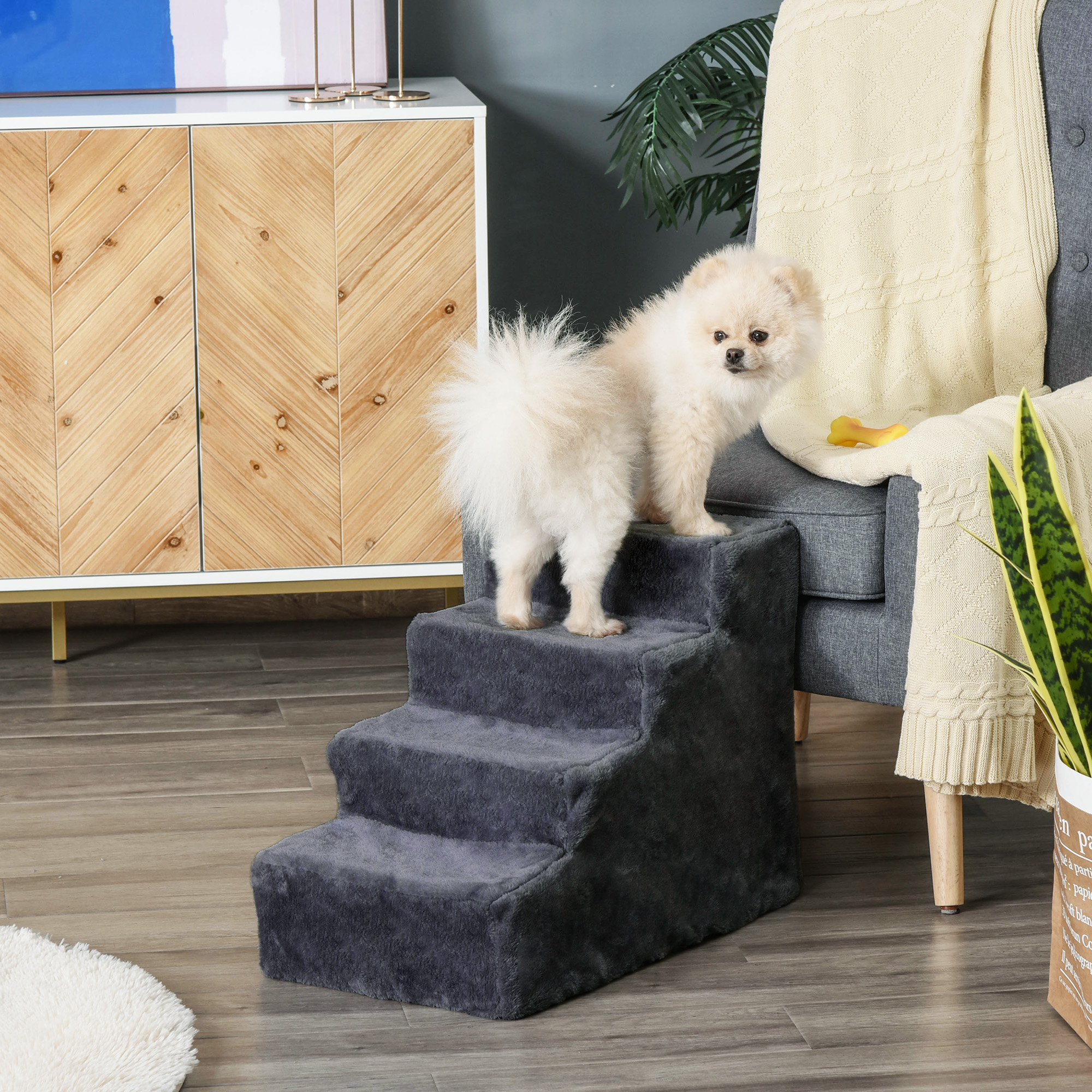 Perro pequeño en escaleras grises para mascotas. El perro está de pie en el escalón superior. Un sofá en el fondo.