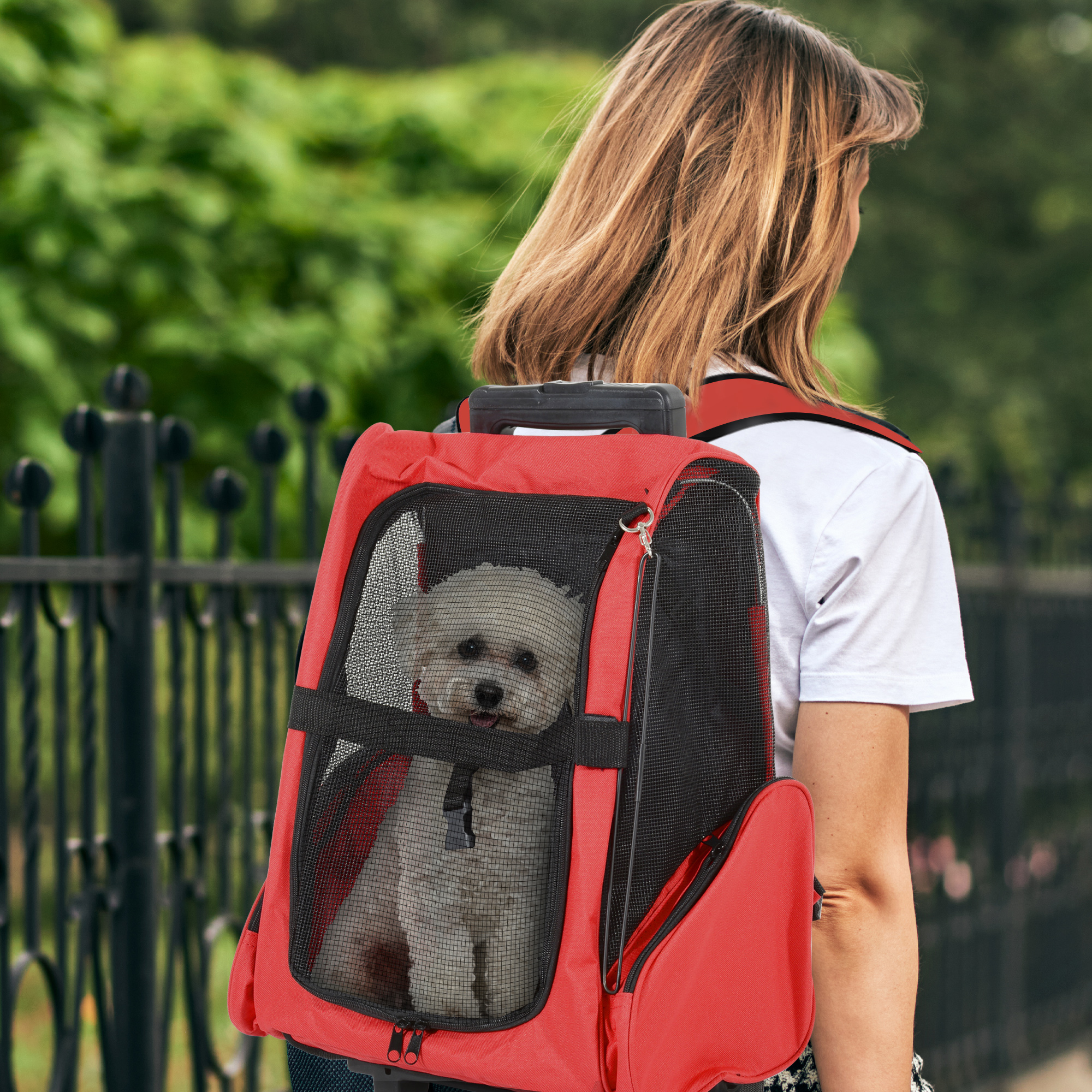 Mujer que lleva una mochila roja para mascotas con un perro blanco dentro, al aire libre.