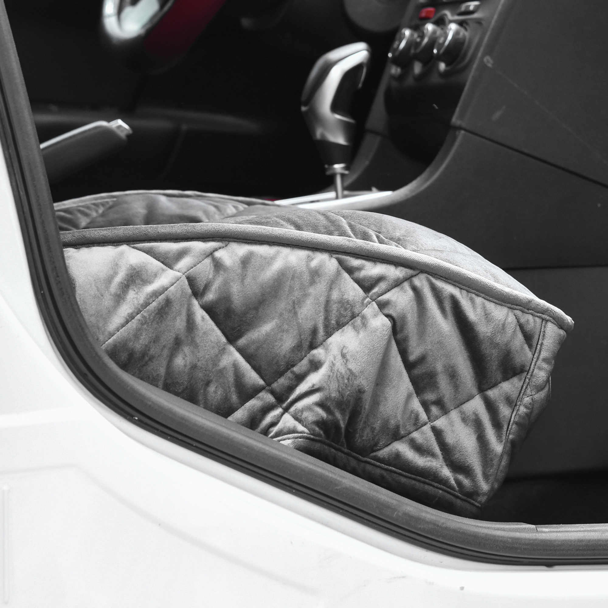 Una funda de asiento acolchada gris para mascotas está instalada en un asiento de automóvil. El interior del automóvil es visible.