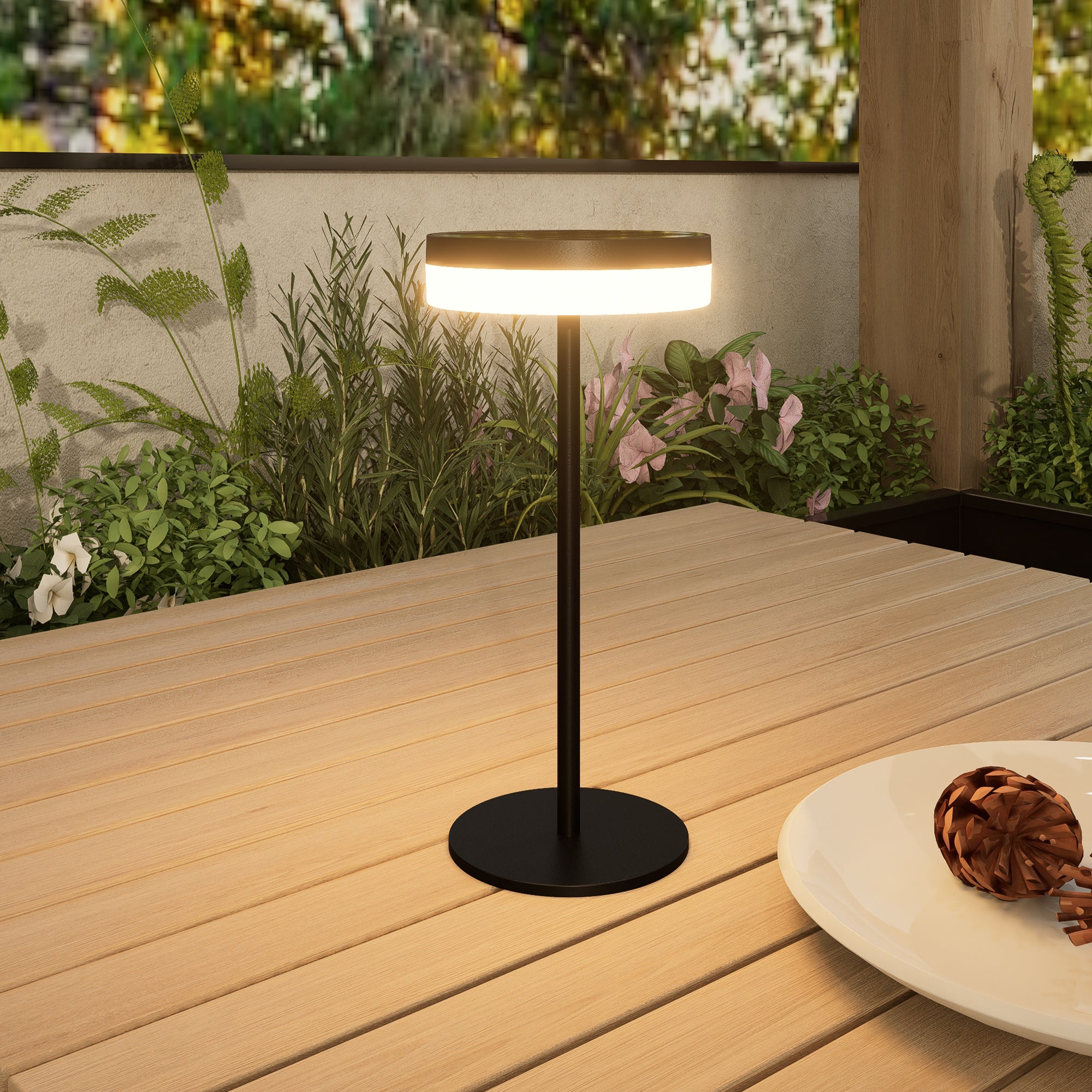 Schwarze Außenlampe auf einem Holztisch, mit Pflanzen und Blumen im Hintergrund.