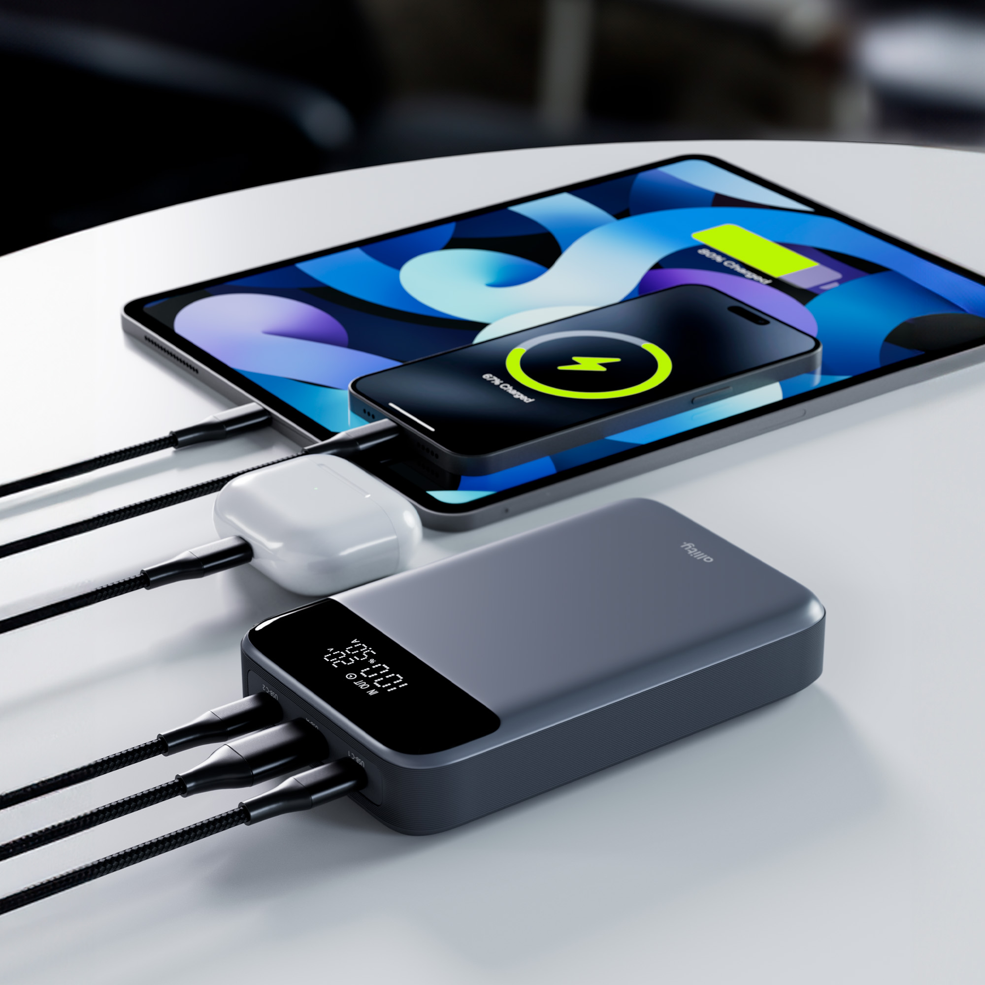 Tablet i telefon ładujące się na białym stole, obok powerbanku i białych akcesoriów.