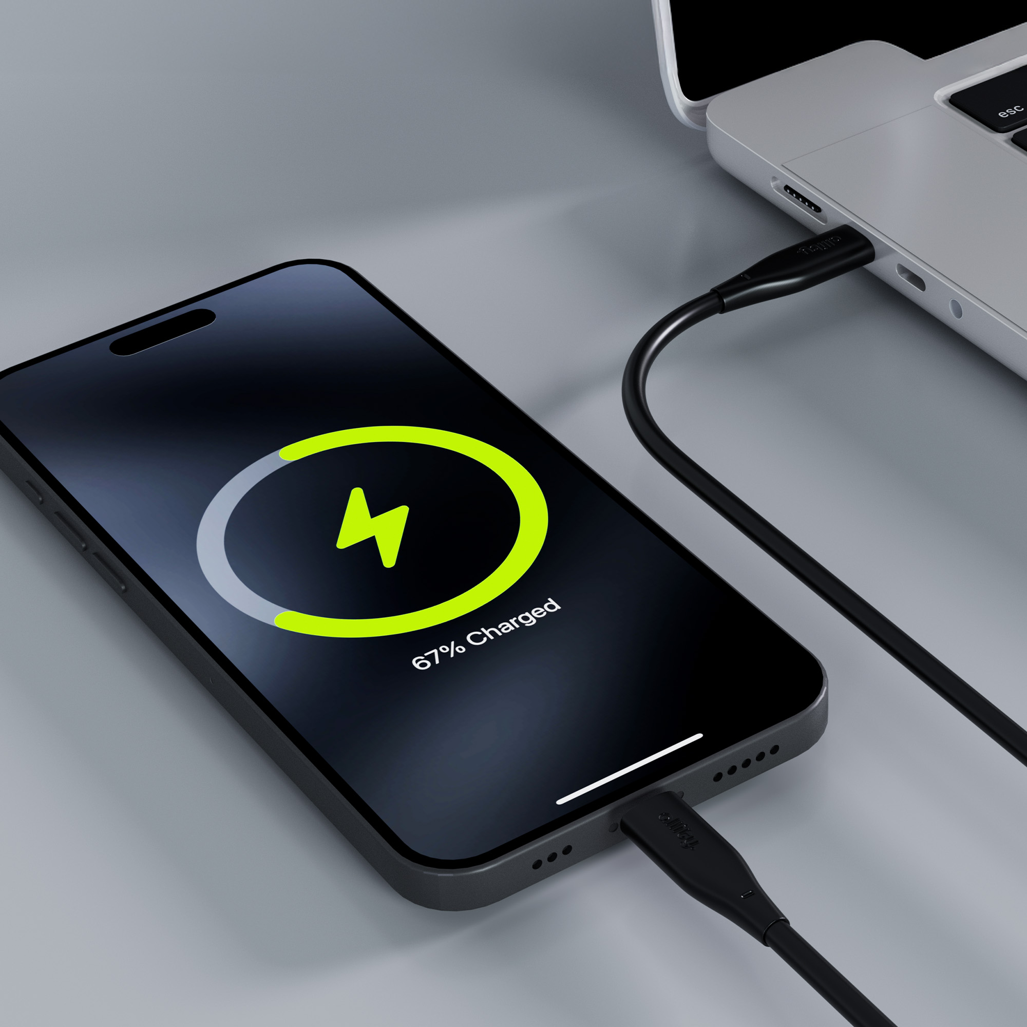 Czarny telefon ładuje się z laptopa. Ekran pokazuje 67% naładowania. Kabel ładujący jest podłączony.