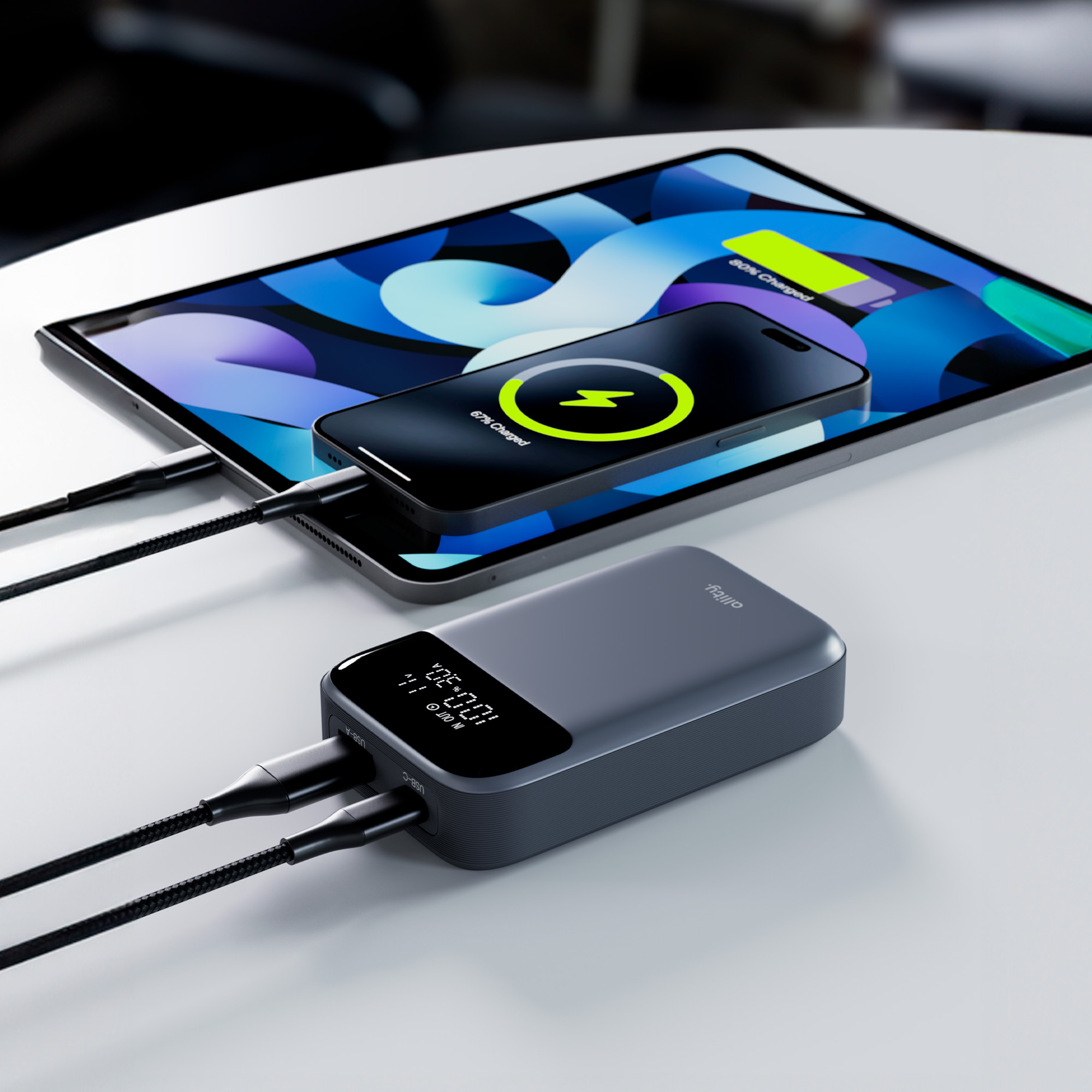 Power bank ładujący telefon i tablet na białej powierzchni. Oba urządzenia pokazują ładowanie.