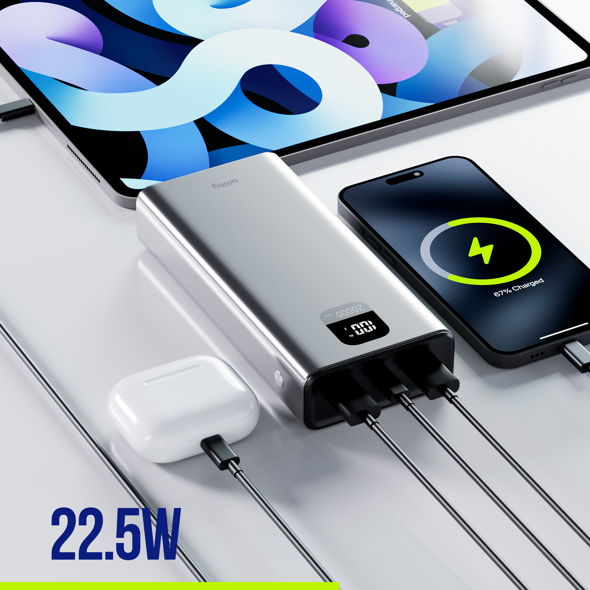 Srebrny power bank ładujący telefon i słuchawki. Telefon pokazuje 67% naładowania. Tablet w tle.