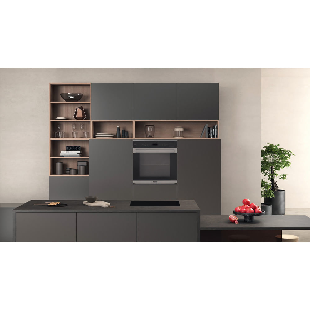 Cucina moderna con forno a incasso, armadi e piano di lavoro. Melograni e una pianta sul bancone.