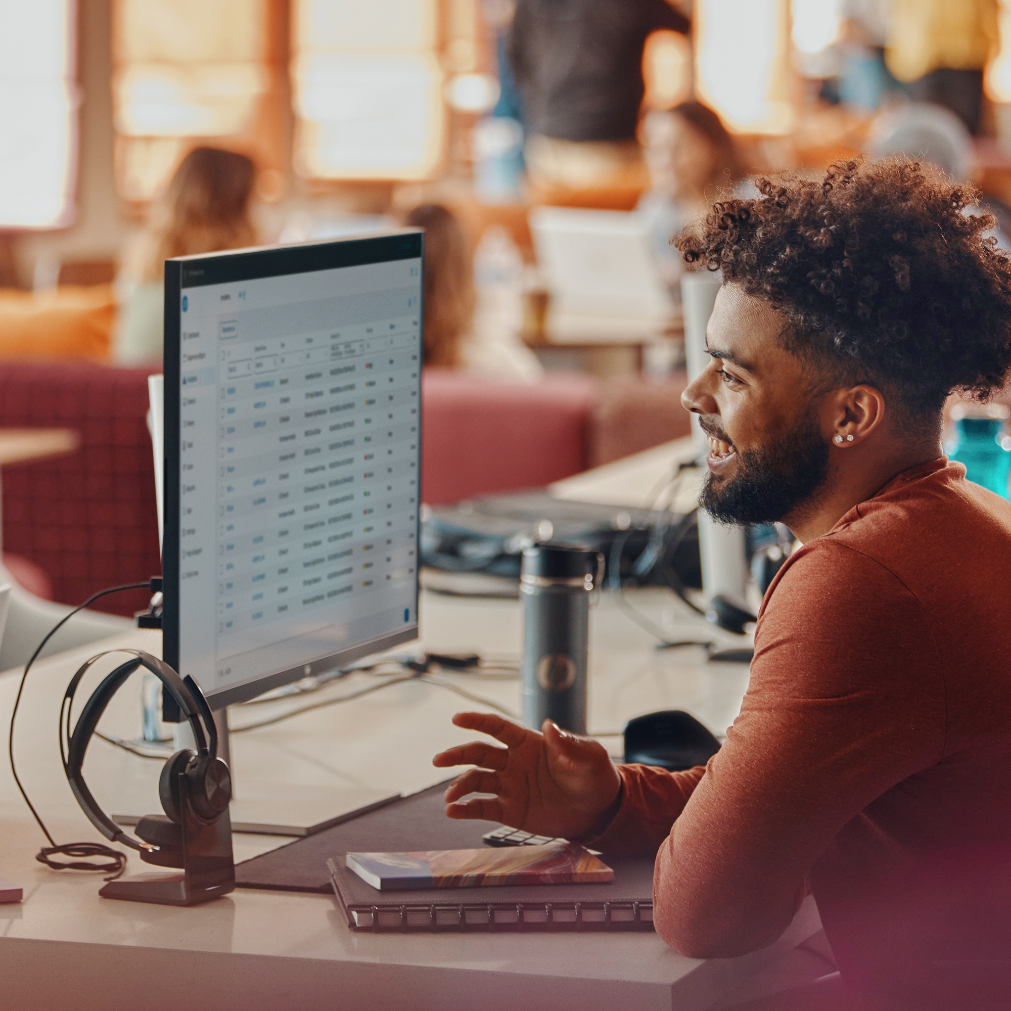 Mężczyzna z kręconymi włosami uśmiecha się, patrząc na ekran komputera.