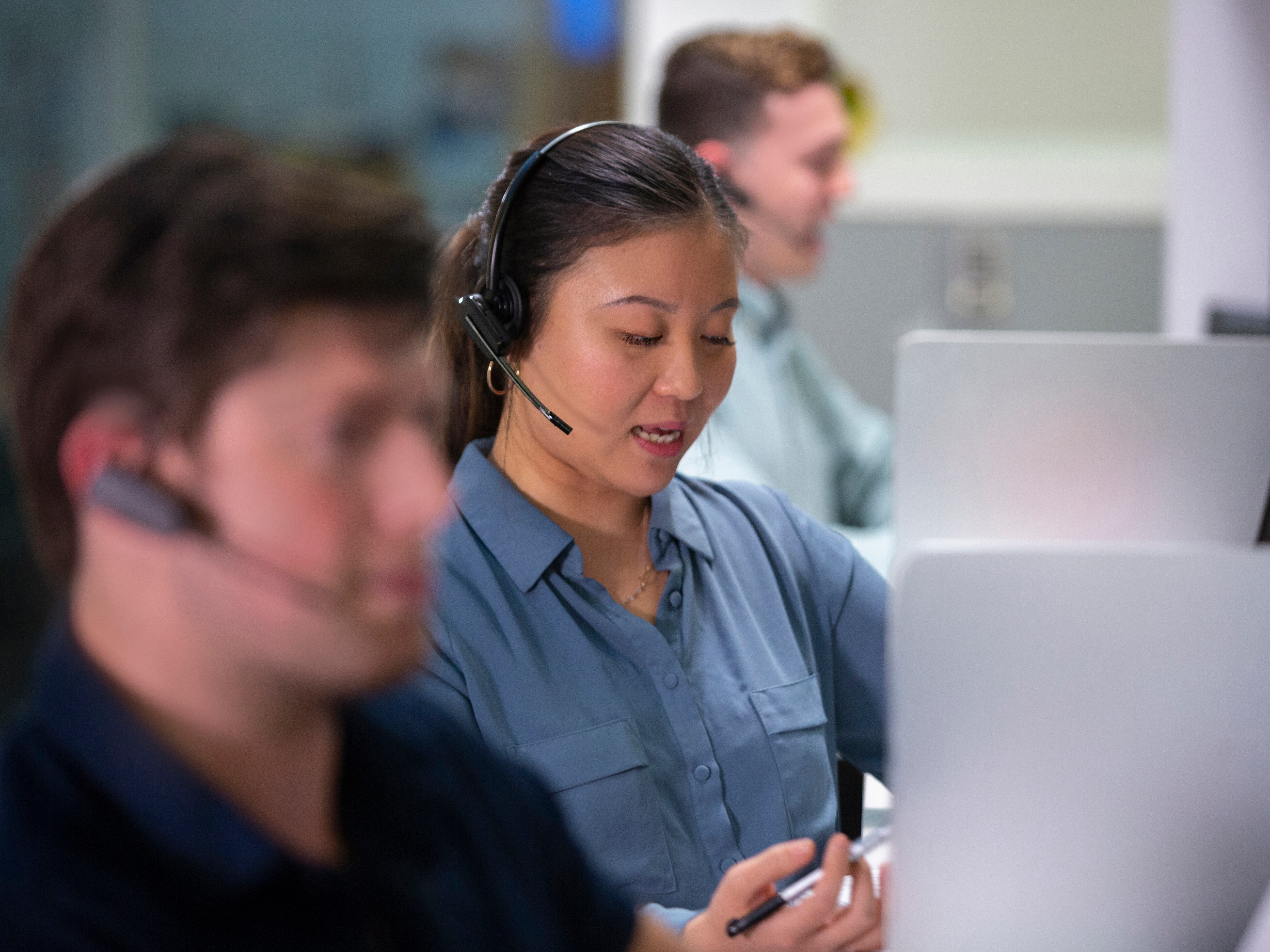 Tre persone con cuffie che lavorano in un ambiente d'ufficio, concentrate sugli schermi.
