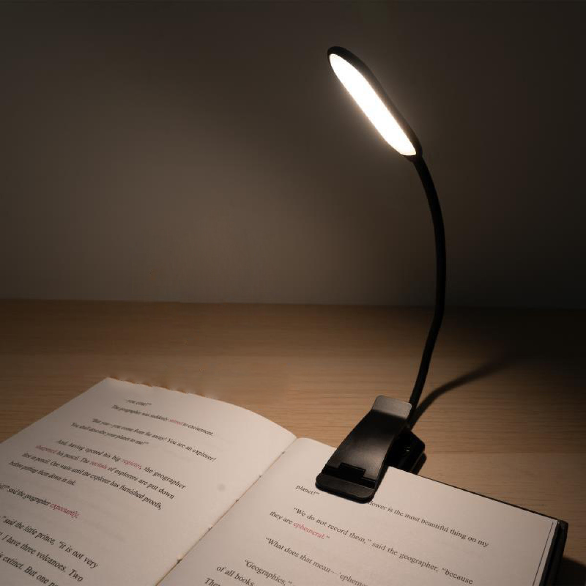 Czarna lampka do czytania przypięta do książki, oświetlająca otwarte strony.