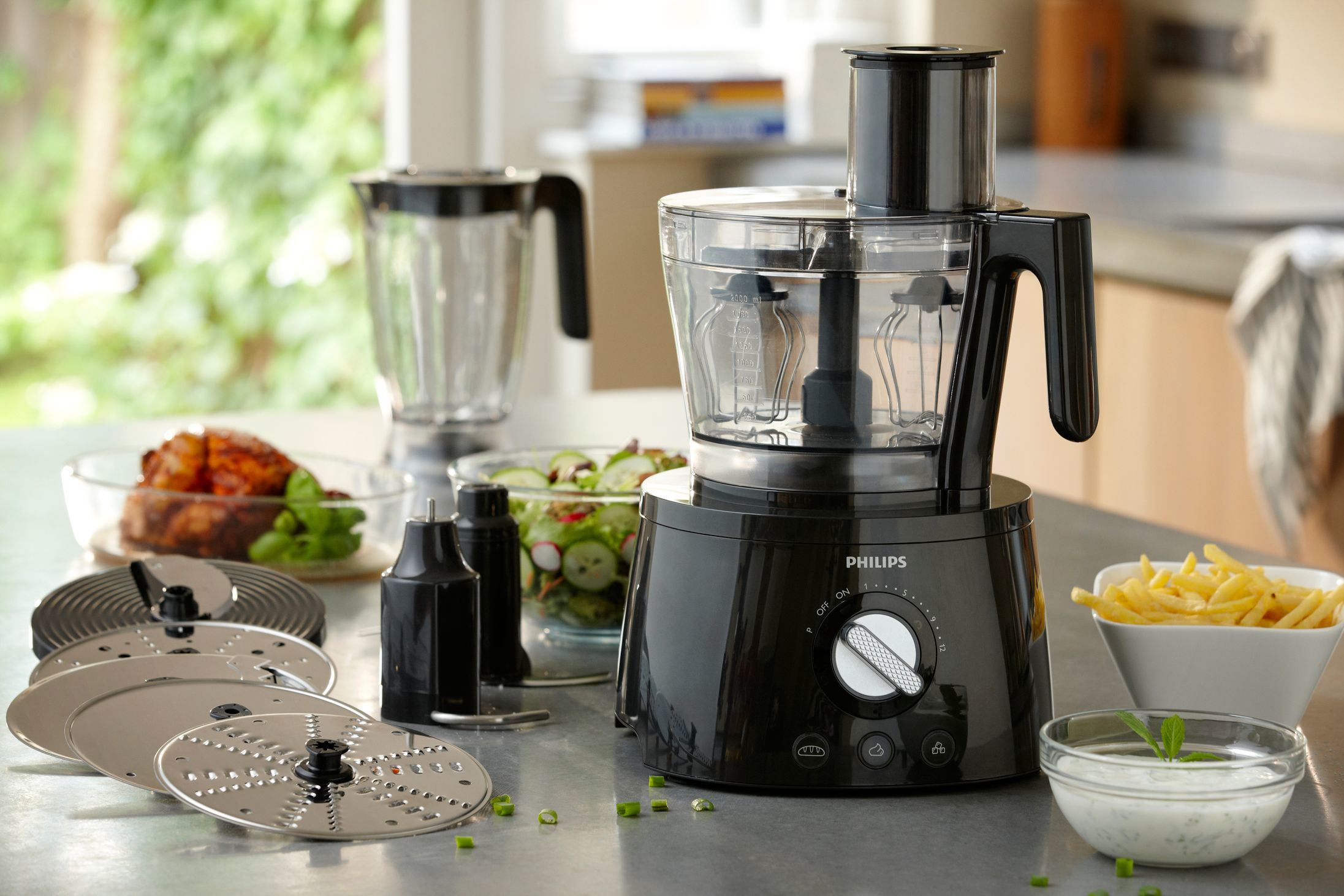 Czarny robot kuchenny Philips z blenderem i akcesoriami na stole. Jedzenie dookoła.