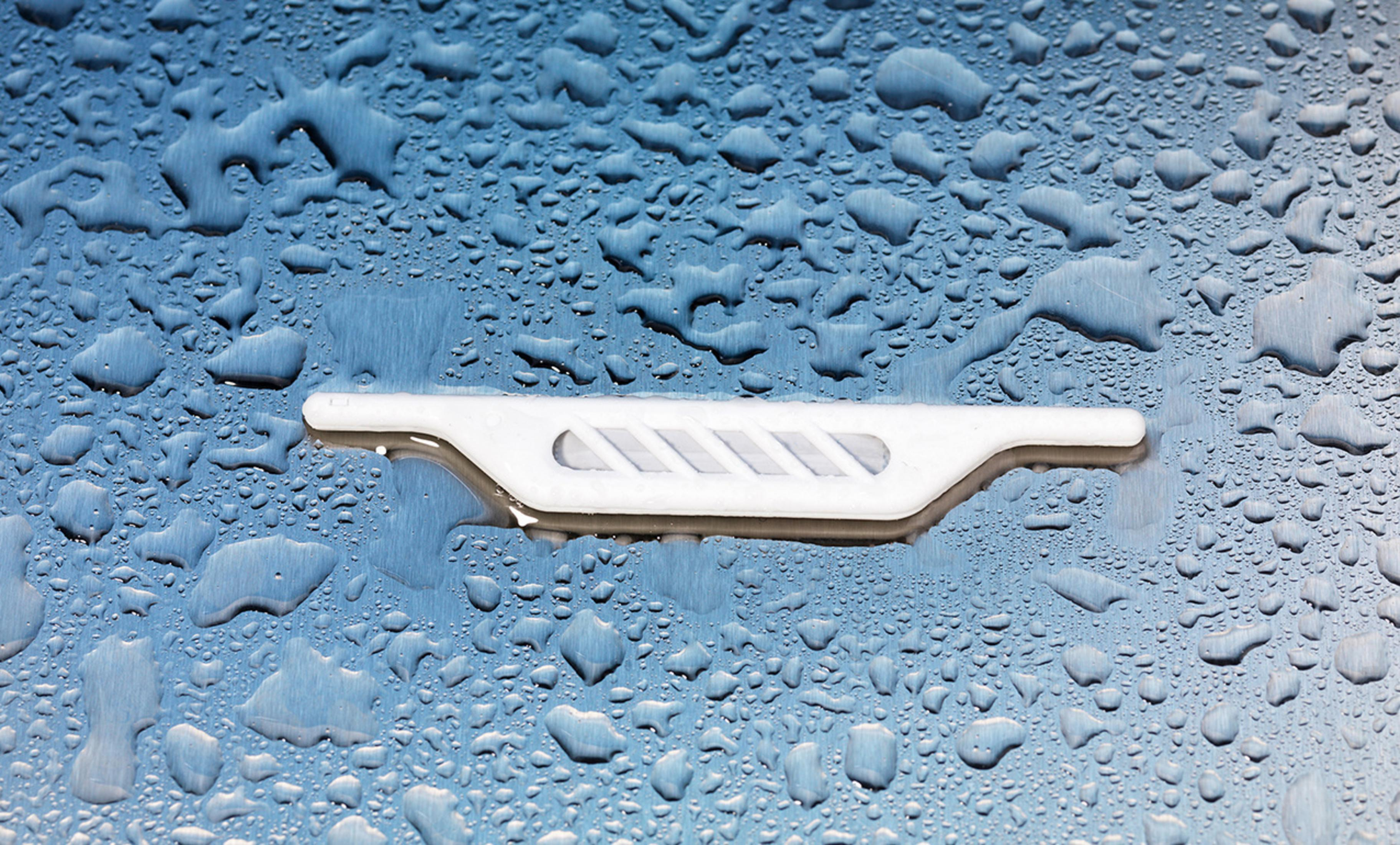 Pièce plastique blanche sur surface bleue avec gouttelettes d'eau. Design incurvé unique.
