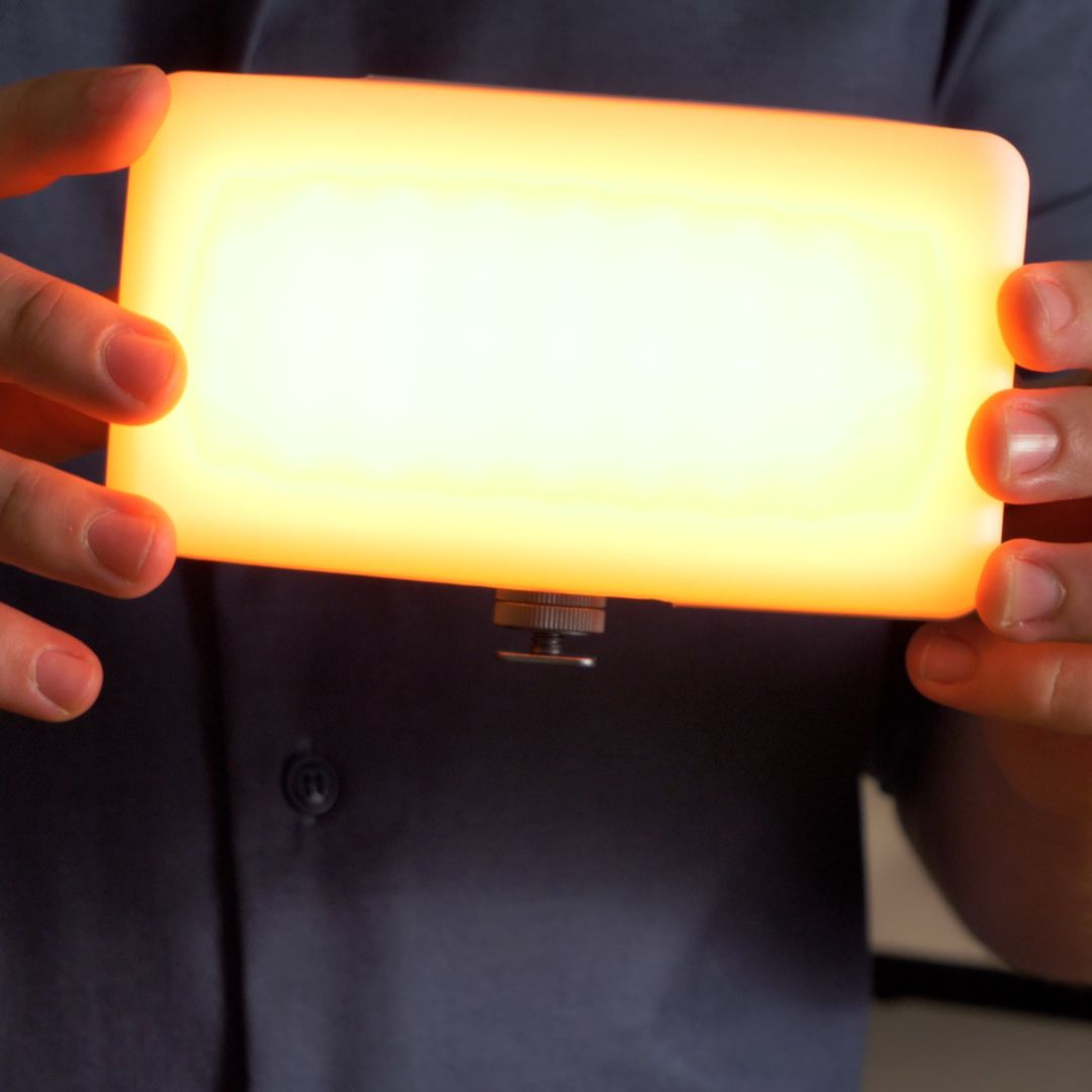 Handen die een helder, rechthoekig, oranje LED-licht vasthouden.