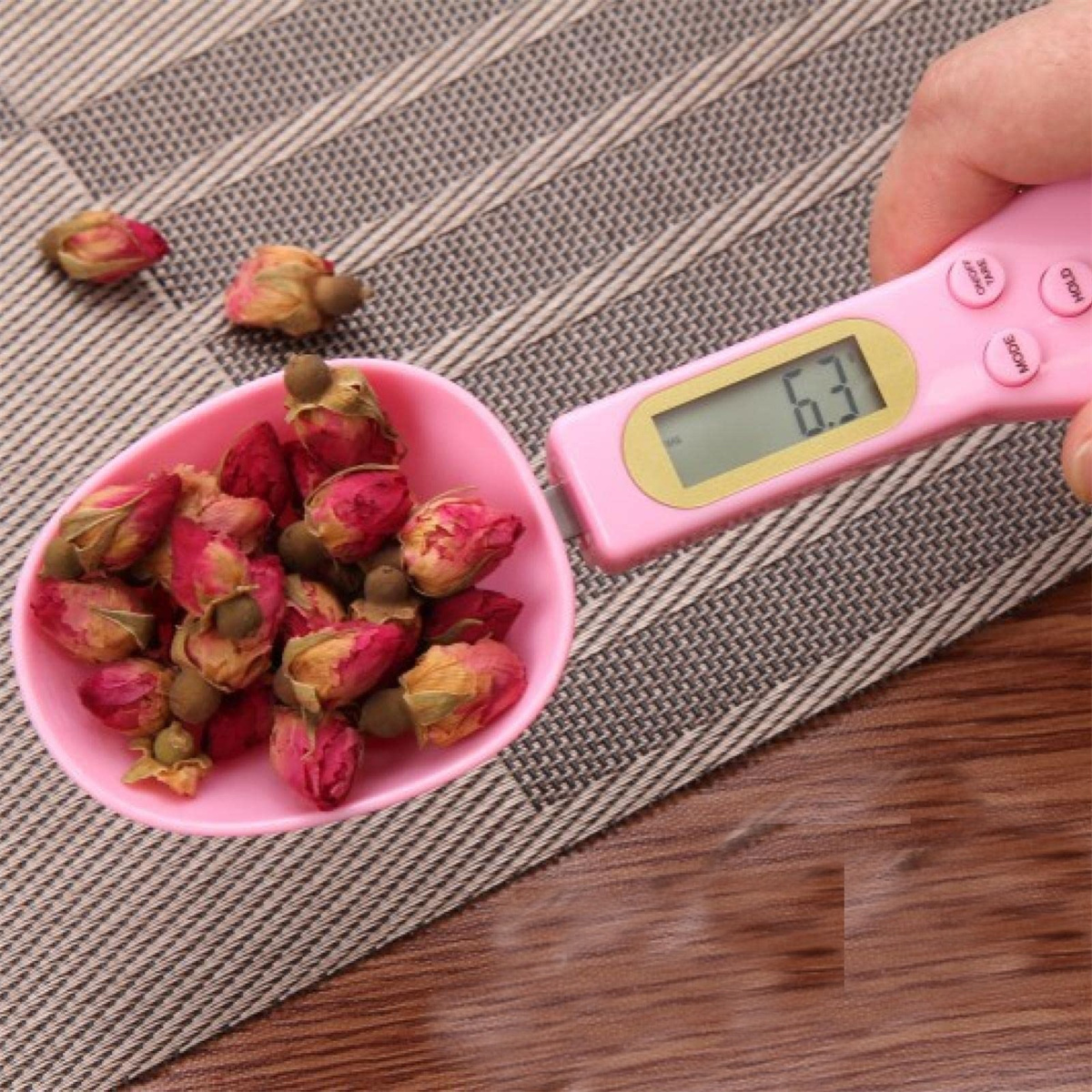 Ein rosa Löffel mit getrockneten Rosenknospen, neben einer rosafarbenen Digitalwaage mit 6,3.