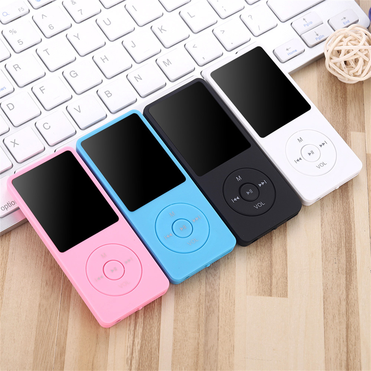 Vier MP3-Player: rosa, blau, schwarz und weiß. Sie liegen auf einem Holztisch neben einer Tastatur.