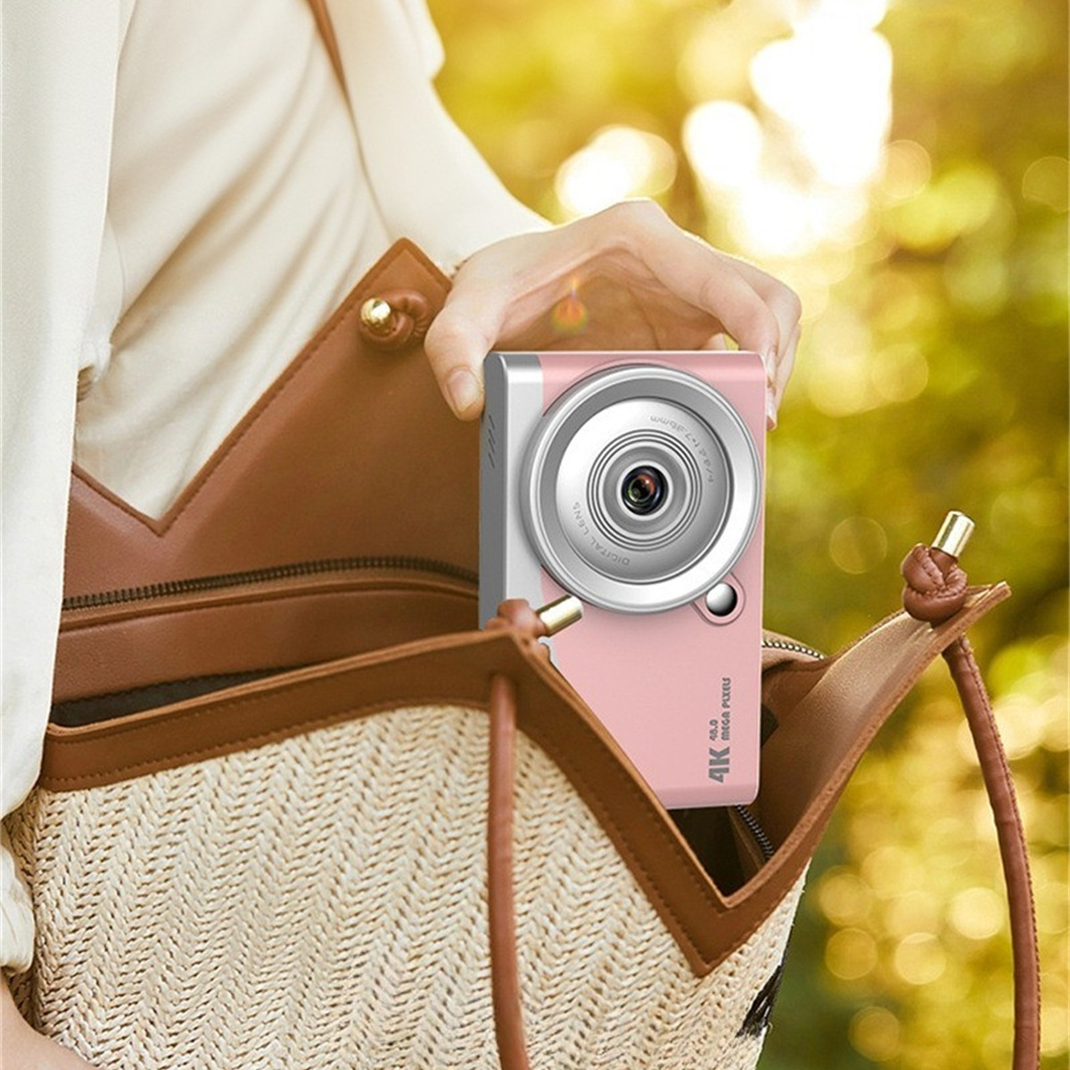 Eine rosa Kamera wird in einer braunen gewebten Tasche gehalten, eine Hand sichtbar.