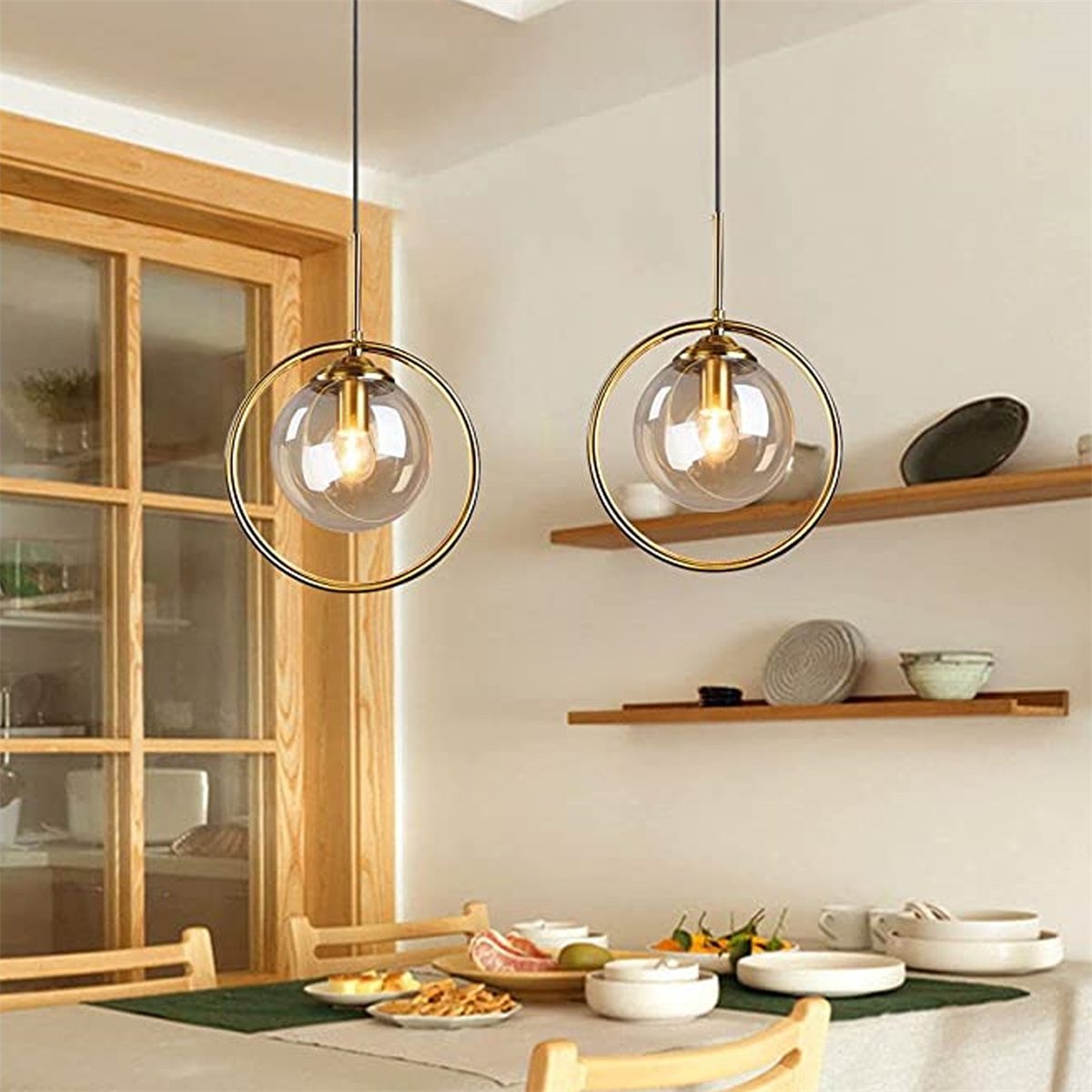 Zwei Pendelleuchten mit goldenen Ringen und klaren Glaskugeln. Der Raum hat einen Tisch und Regale.