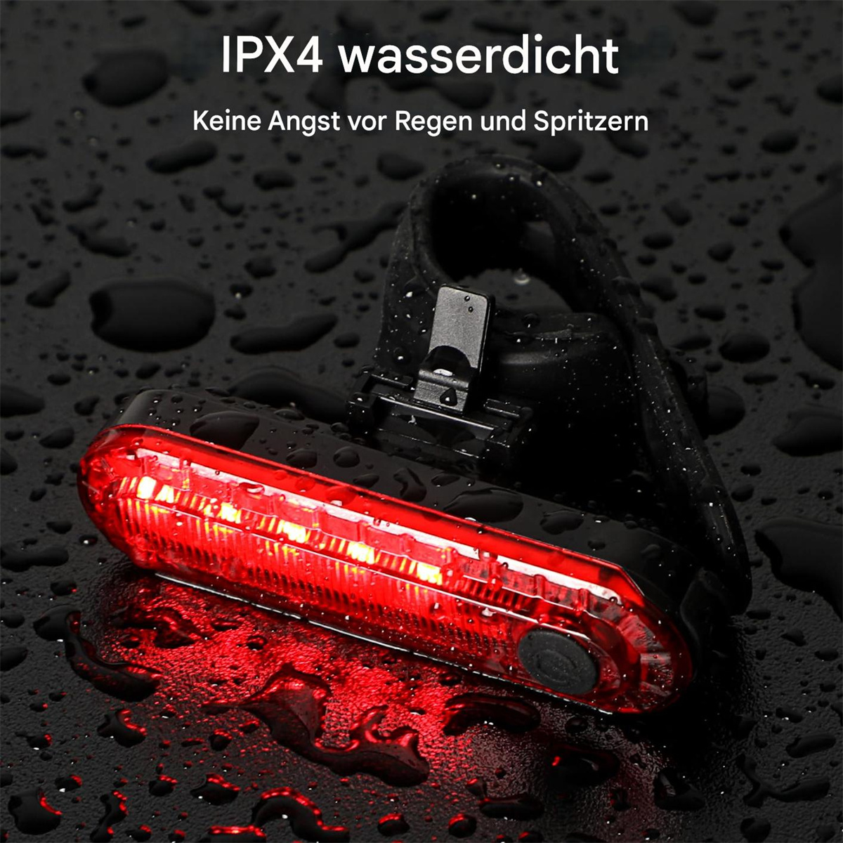 Ein rotes LED-Fahrradlicht liegt auf einer schwarzen, nassen Oberfläche mit Wassertropfen.