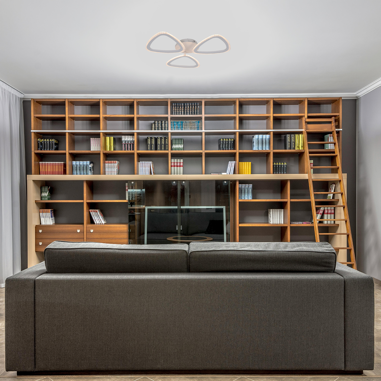 Soggiorno con divano grigio scuro, libreria piena di libri e scala in legno.