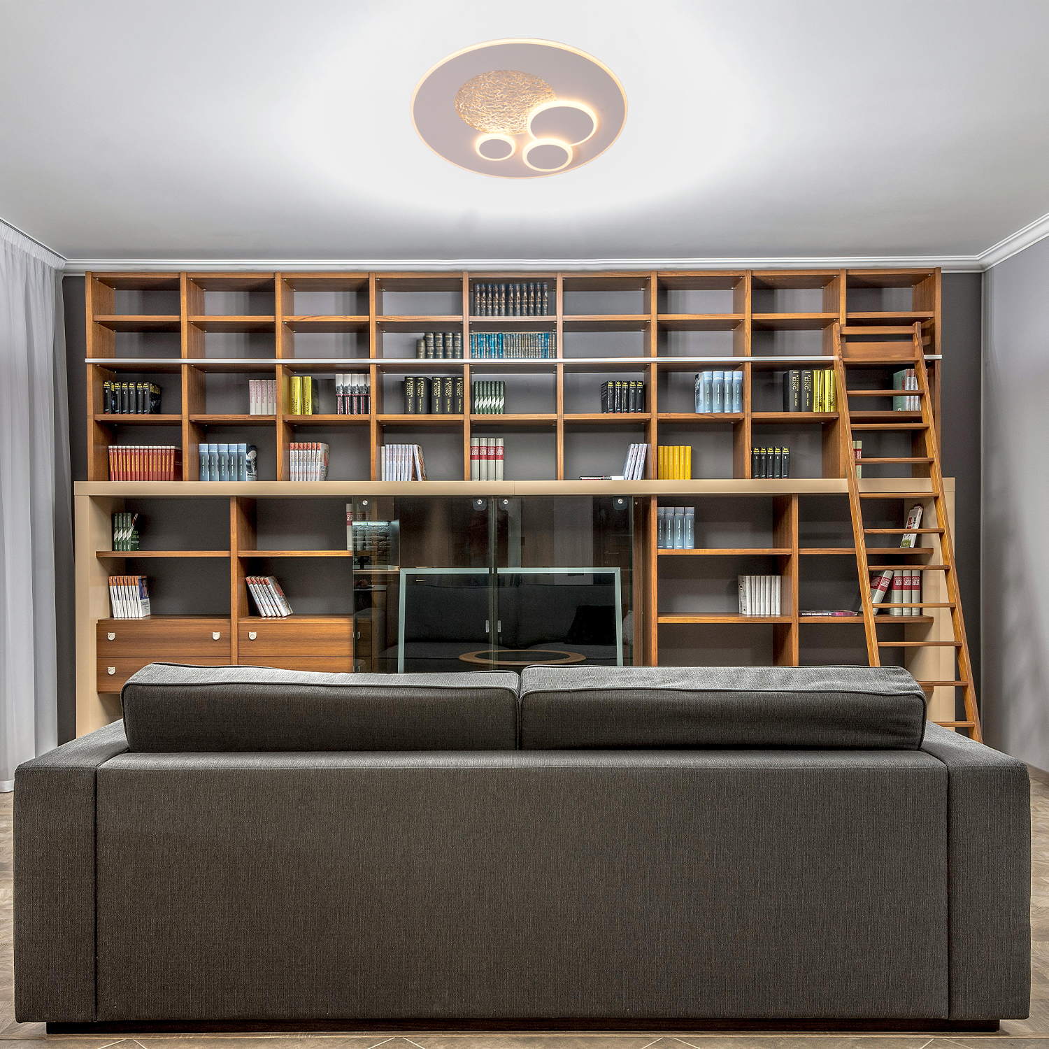 Una stanza con una grande libreria in legno, un divano e una lampada da soffitto. La lampada ha un design circolare ed è bianca.