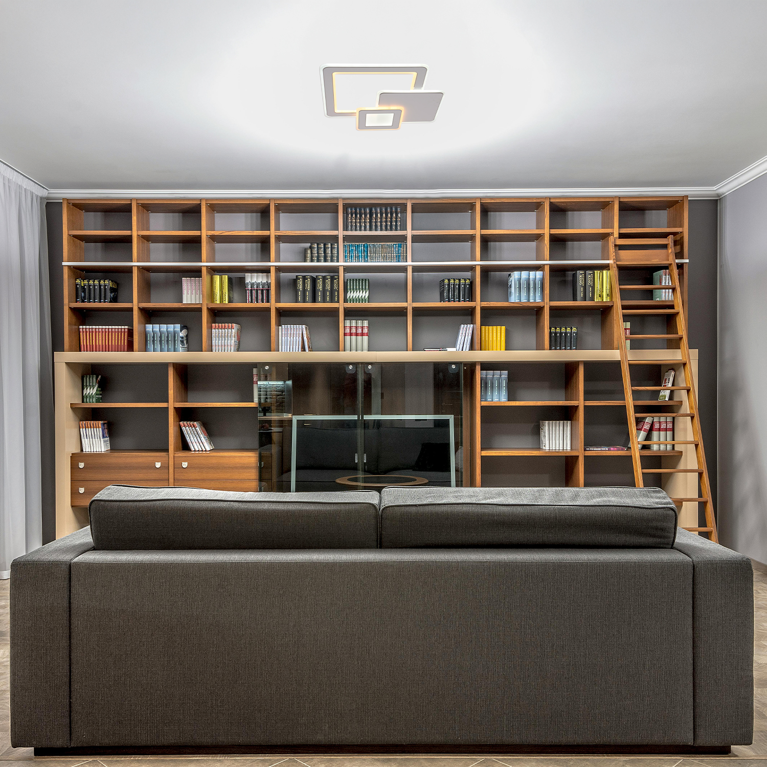 Interno con divano, grande libreria in legno e lampada da soffitto. Scaffali, scala, TV e lampada.