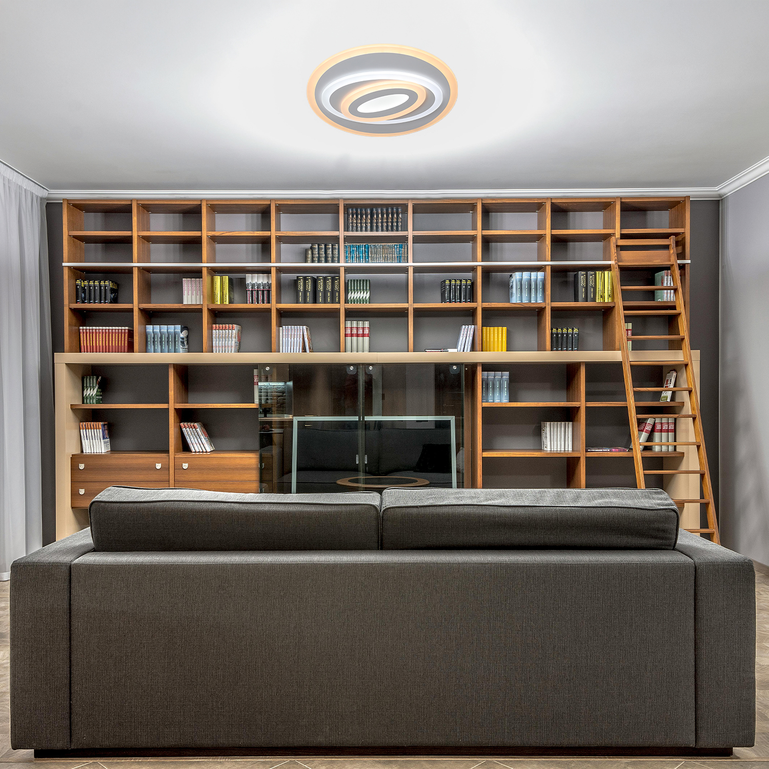 Interno con divano, libreria in legno e lampada da soffitto. Scaffali, scala, TV e lampada circolare.