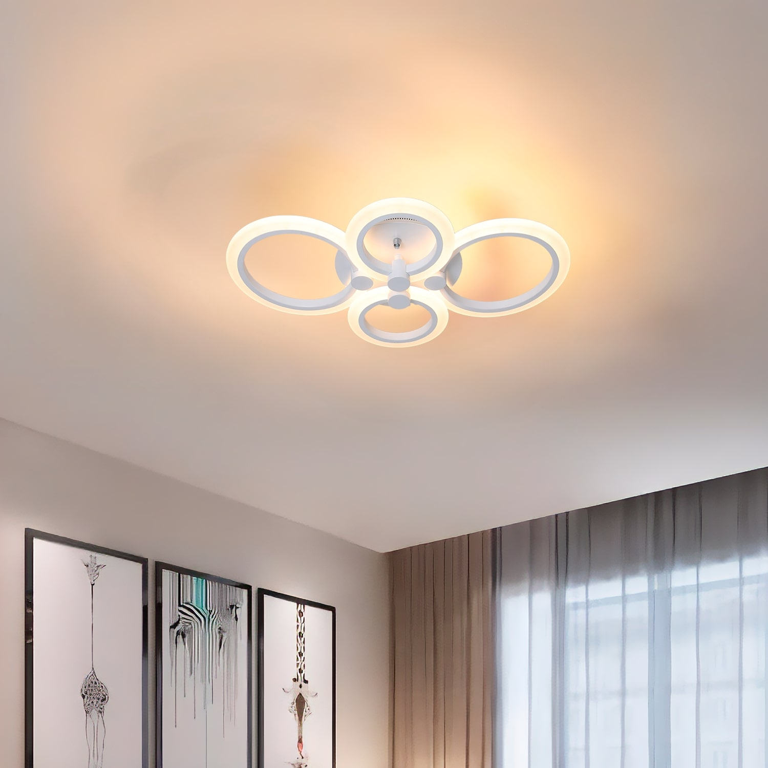 Plafoniera bianca con quattro anelli luminosi interconnessi. La stanza ha opere d'arte e tende.