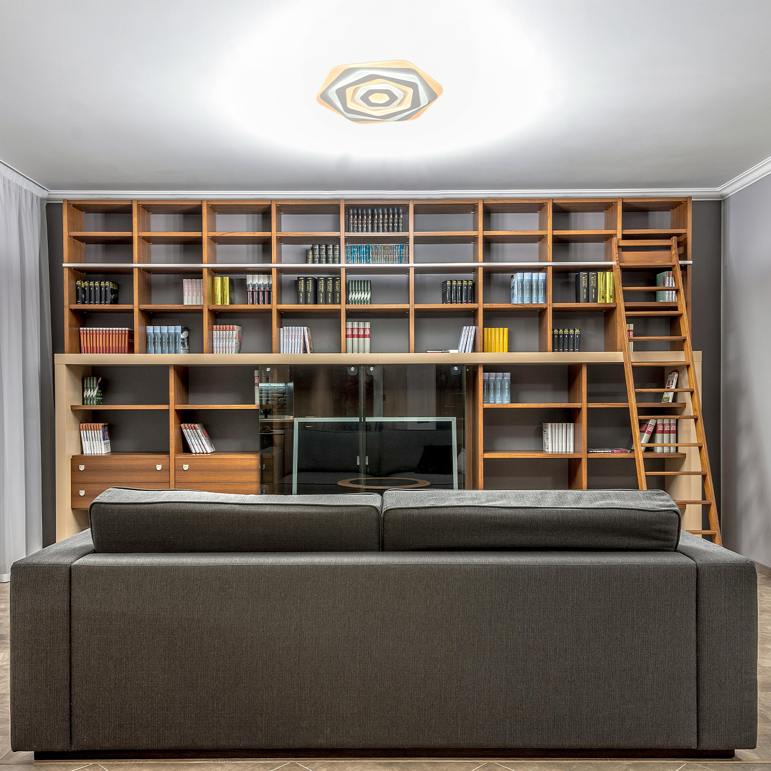 Un soggiorno con libreria, divano e moderna plafoniera, disposta a forma esagonale.