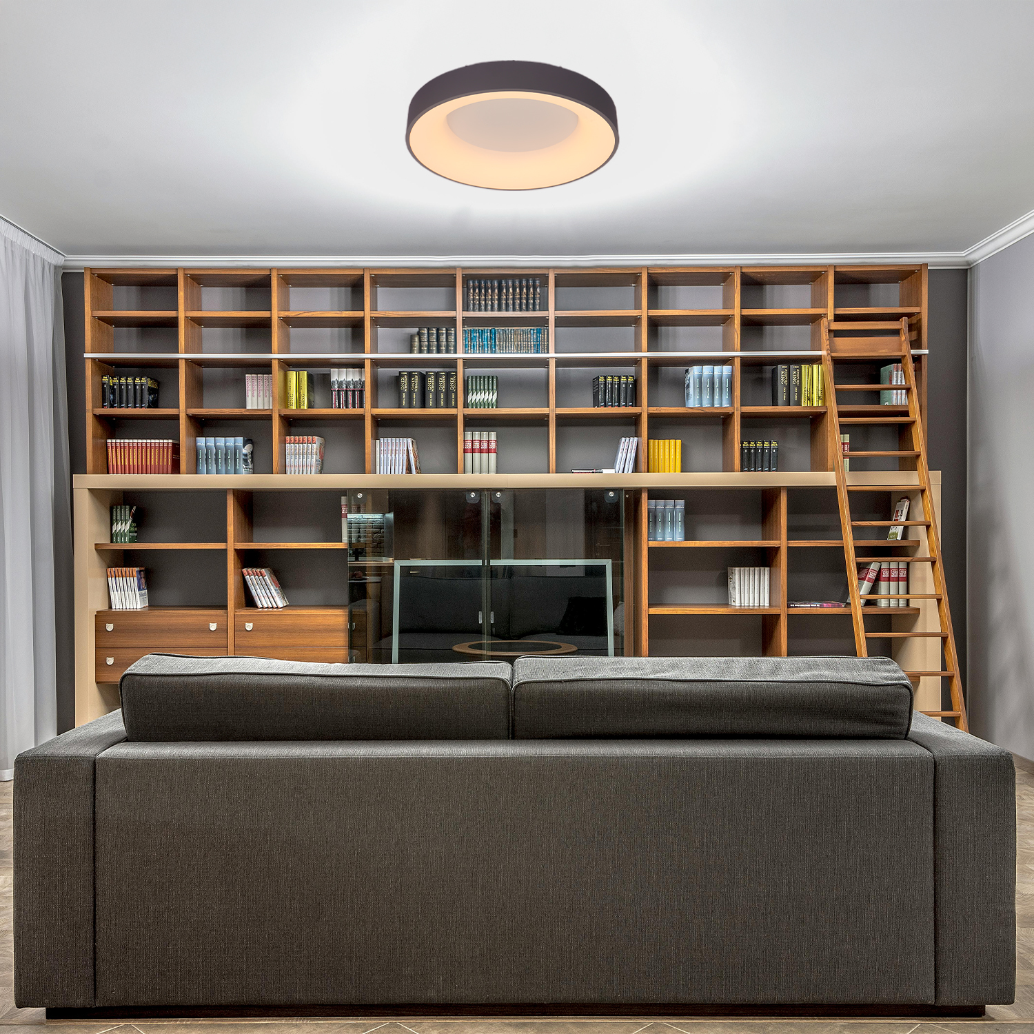 Soggiorno con libreria, divano e lampada da soffitto. Libreria marrone e divano grigio.