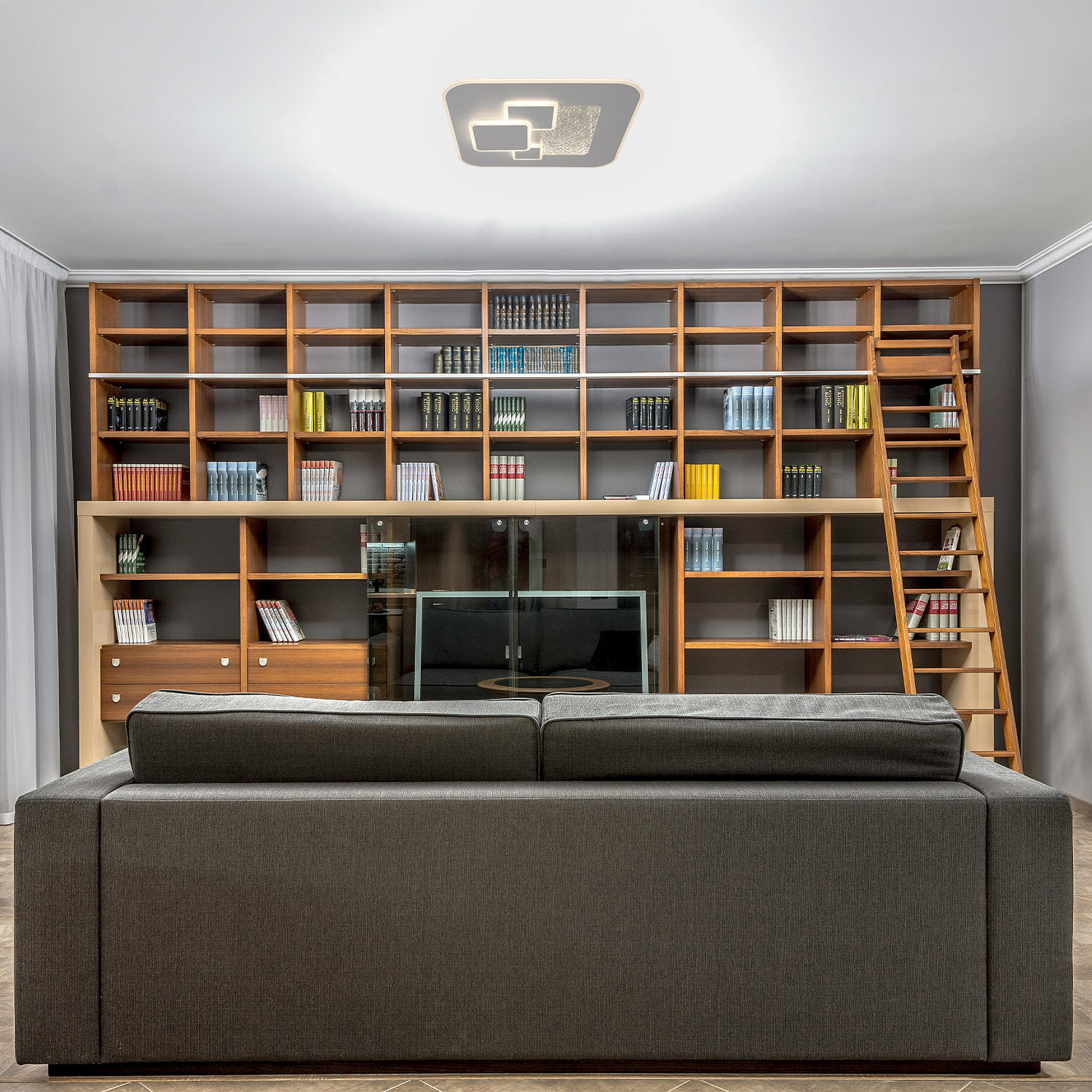 Soggiorno con libreria, divano e lampada da soffitto. Libreria marrone e divano grigio.