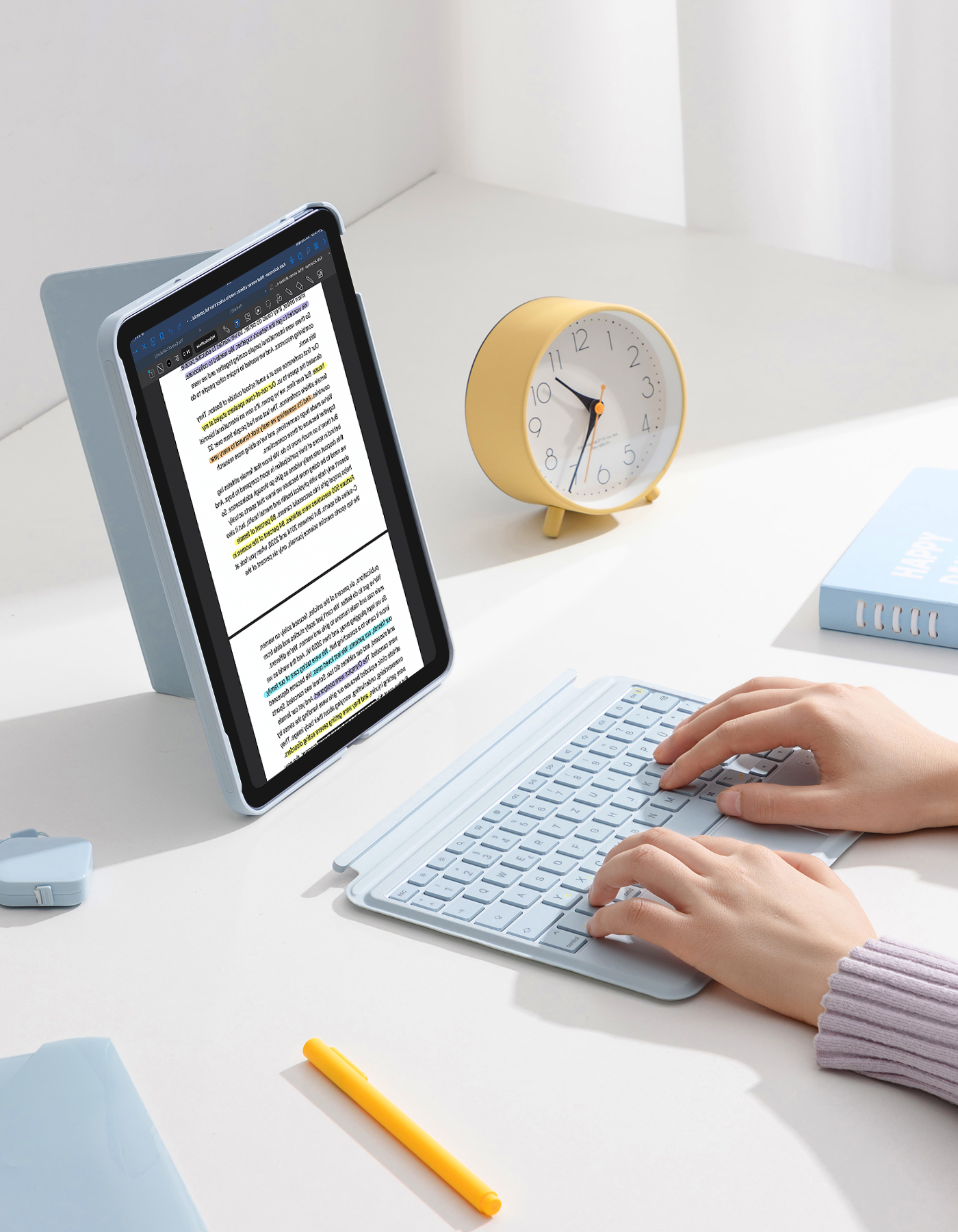 Tablet in hellblauer Hülle auf weißem Schreibtisch. Gelber Wecker und Tastatur auf dem Schreibtisch.