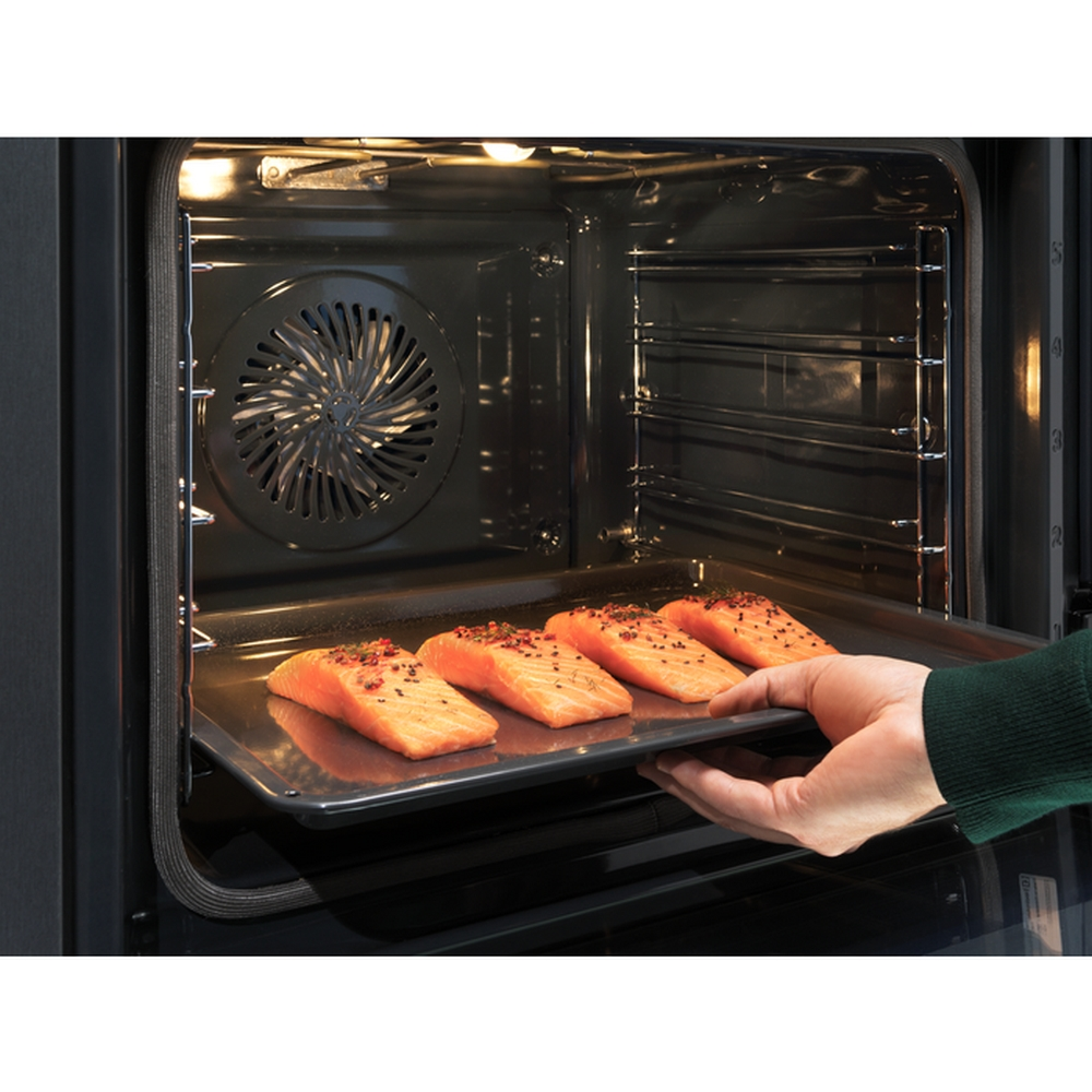Una mano fa scivolare una teglia di salmone in un forno con ventola e griglie.