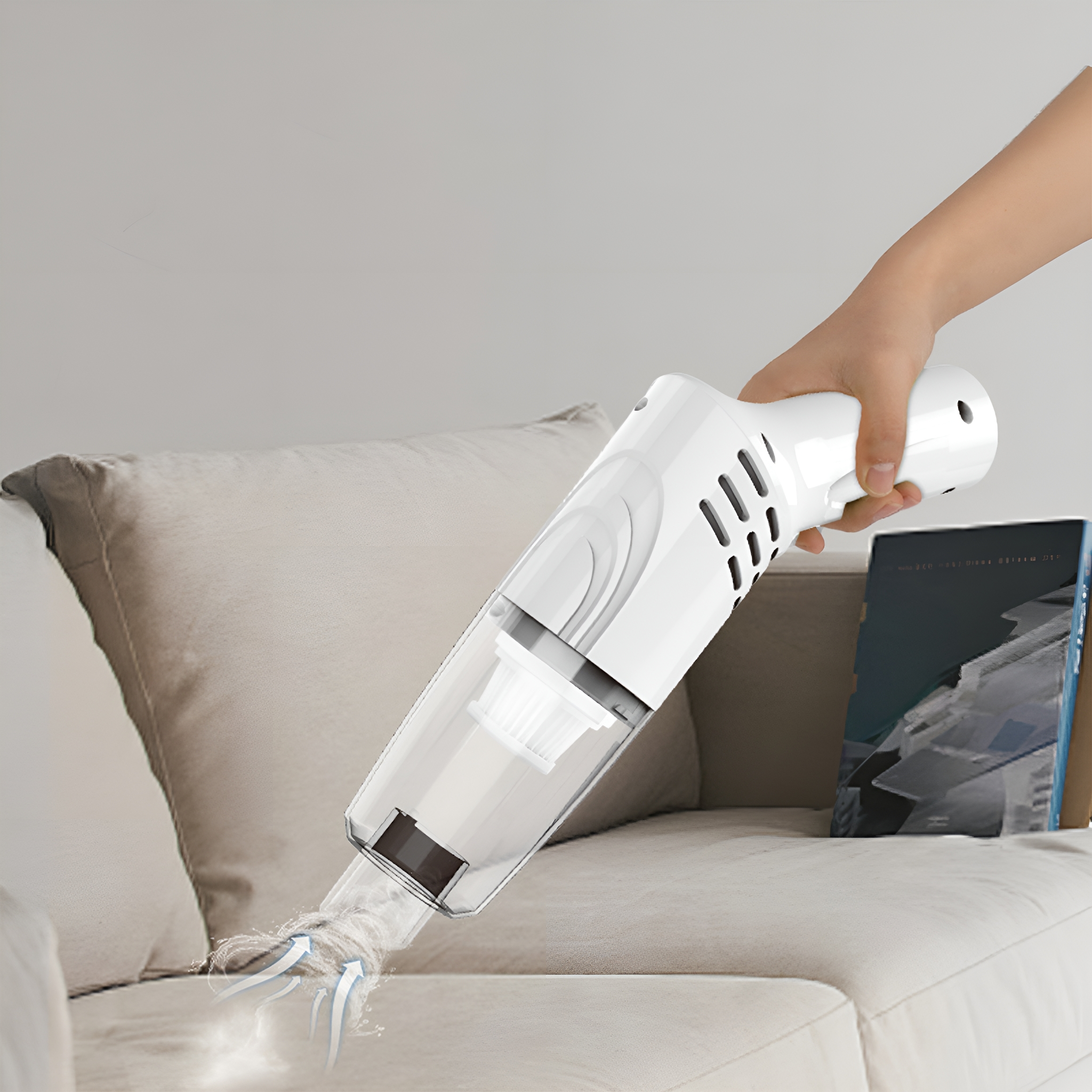 Eine Hand hält einen weißen Staubsauger und reinigt ein Sofa. Der Sauger ist so angewinkelt, dass er Schmutz aufsaugt.