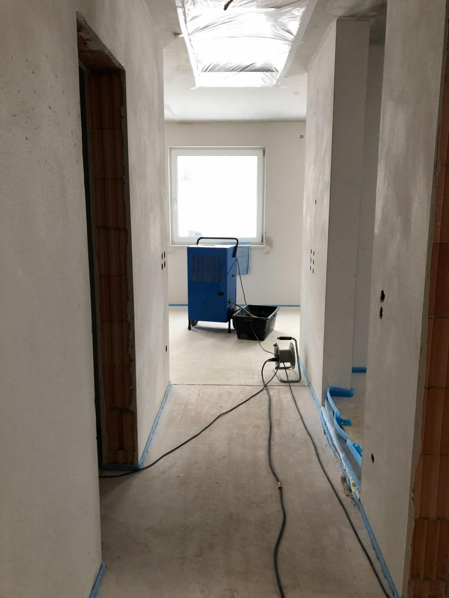 Flur im Bau. Blaues Klebeband auf dem Boden. Blaue Maschine, schwarzer Eimer und Kabel.