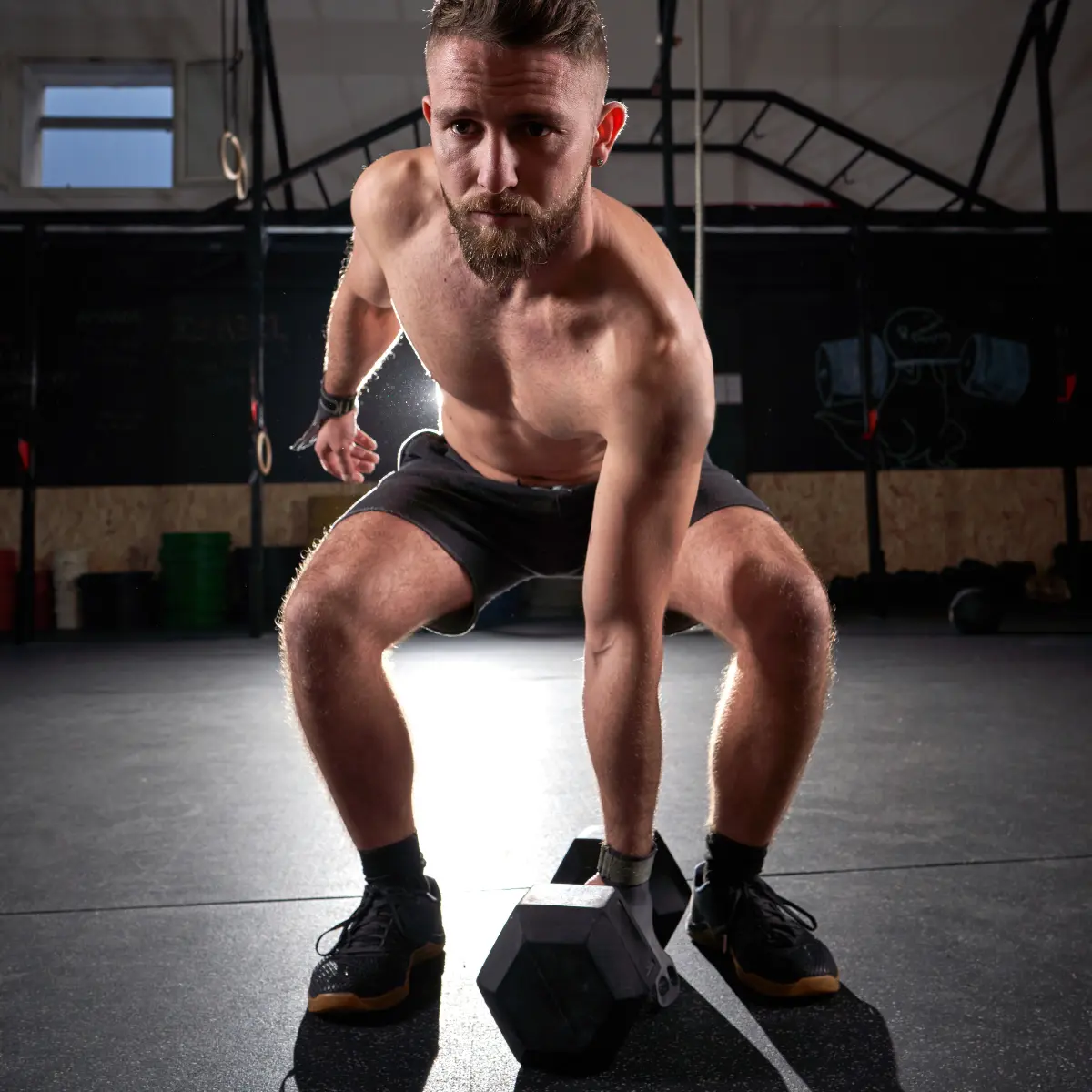 A man in a gym lifting a heavy dumbbell, with focused expression.