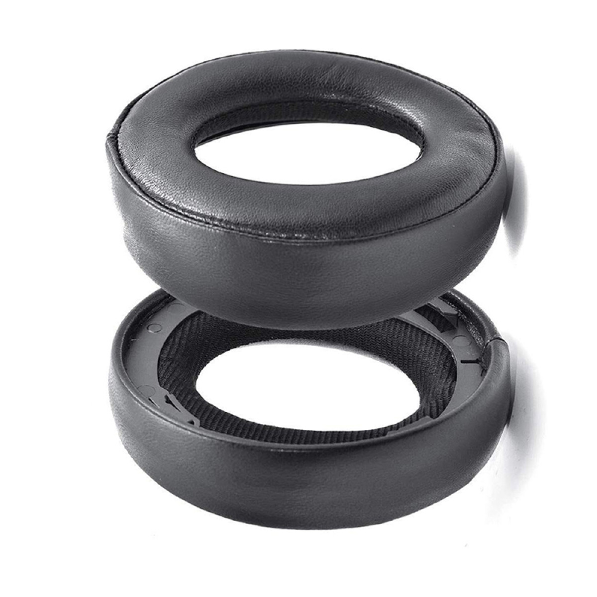 Dwie czarne poduszki nauszne do słuchawek, jedna zdemontowana. Szczegóły na białym tle.