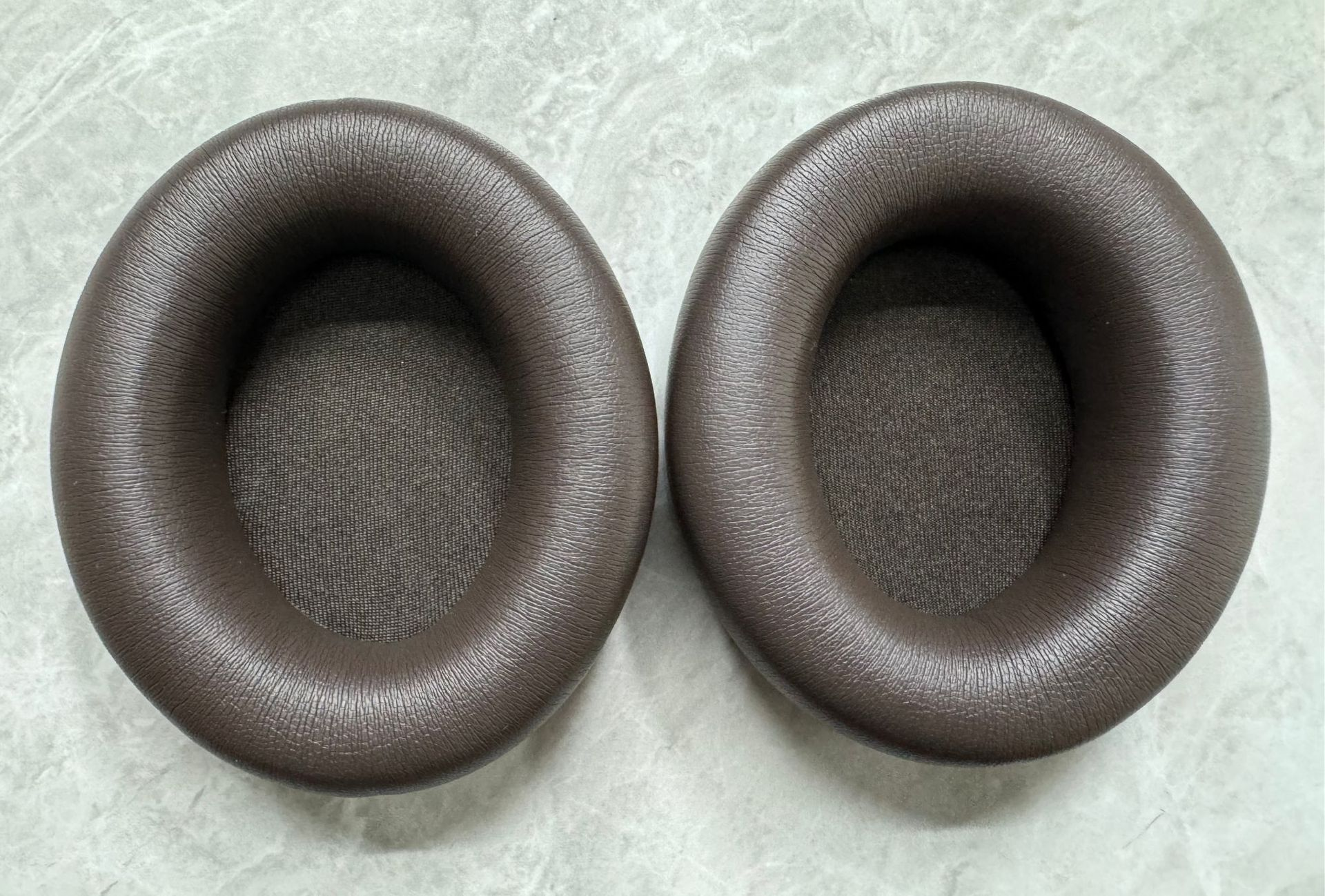 Dwie brązowe, okrągłe poduszki na uszy. Mają fakturę podobną do skóry.