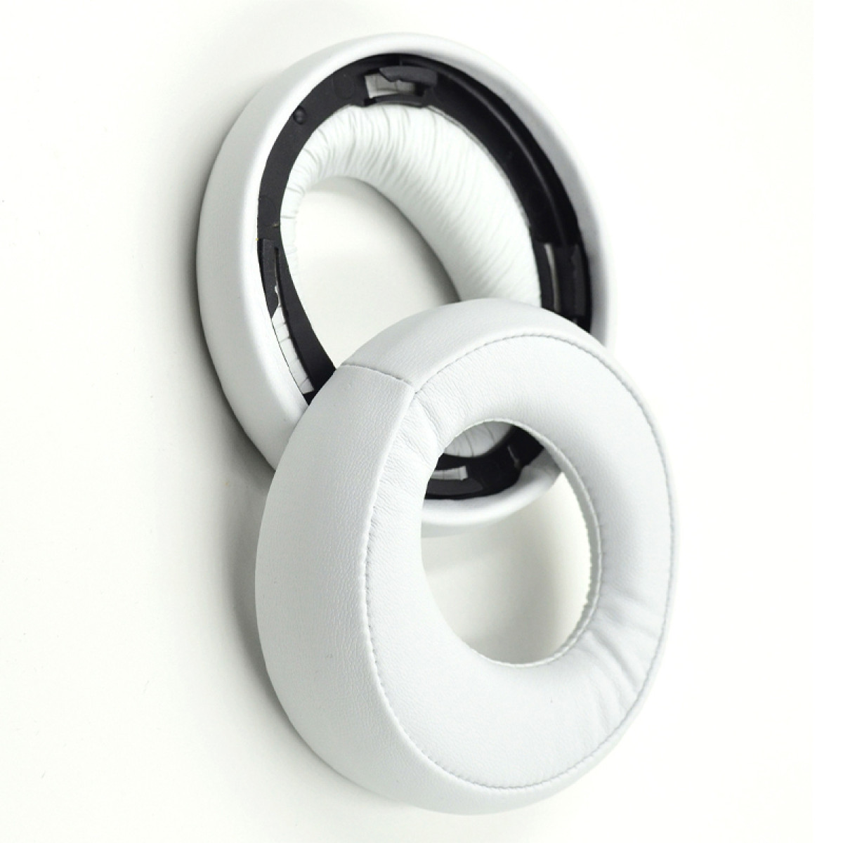 Twee witte oorkussens voor hoofdtelefoons, met zwart interieur. De ene ligt op de andere.