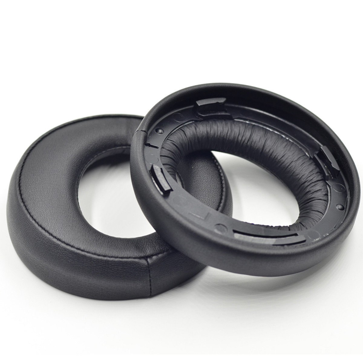Dwie czarne, okrągłe poduszki na uszy na białym tle.