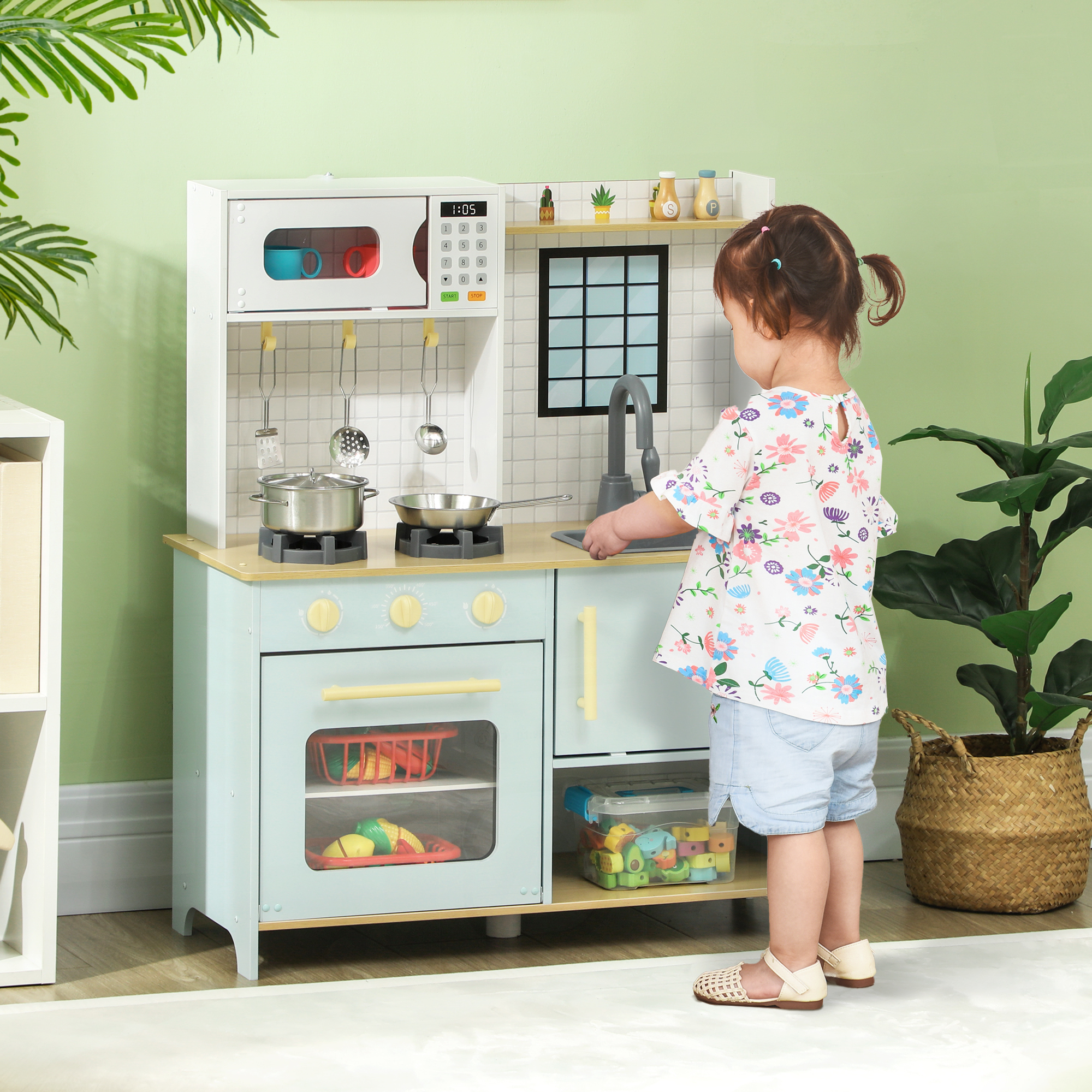 Un niño jugando con una cocina de juguete, colores azul pastel, blanco y madera, en una habitación verde.