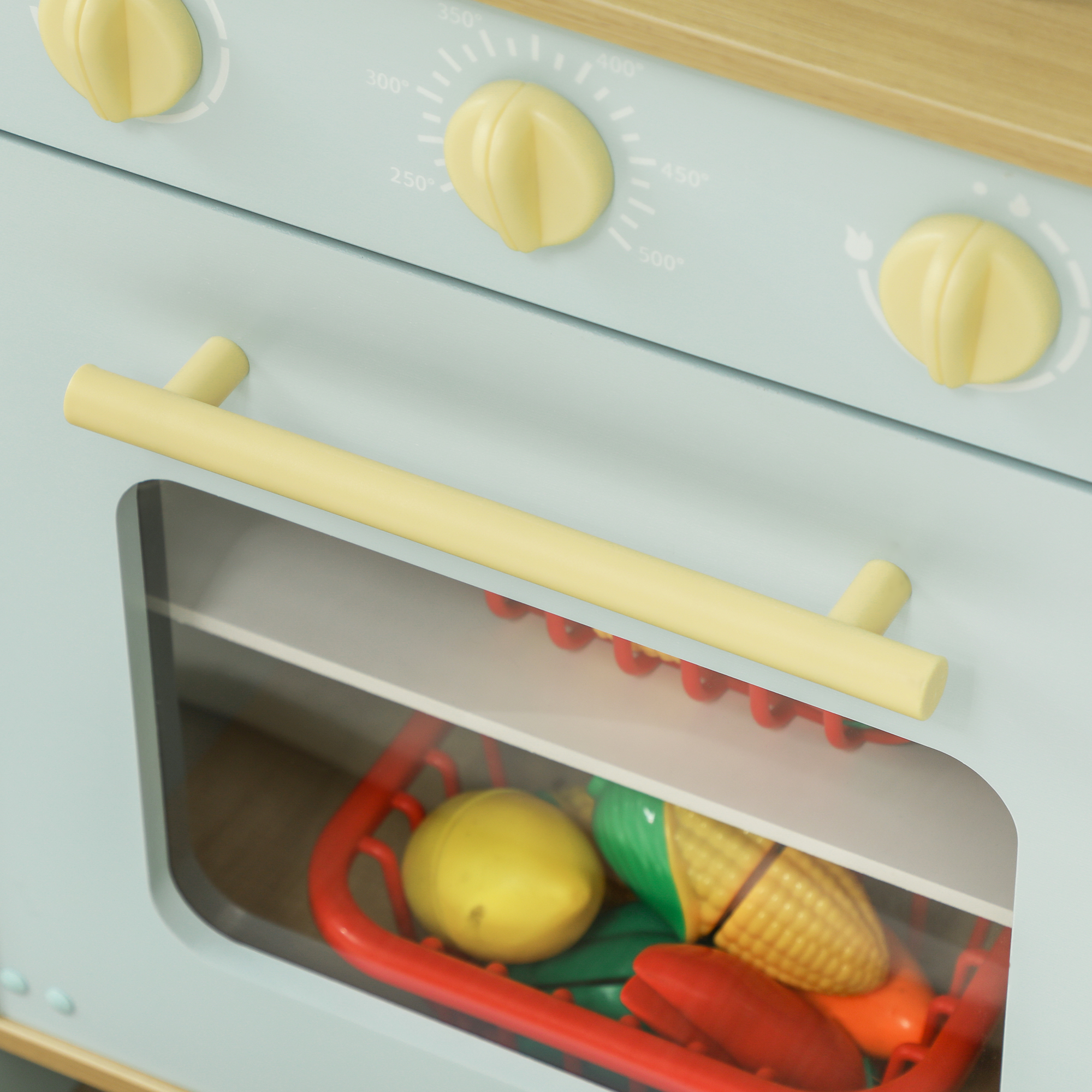 Primer plano de una cocina de juguete azul con detalles del horno: perillas, manija y una cesta de comida de juguete.