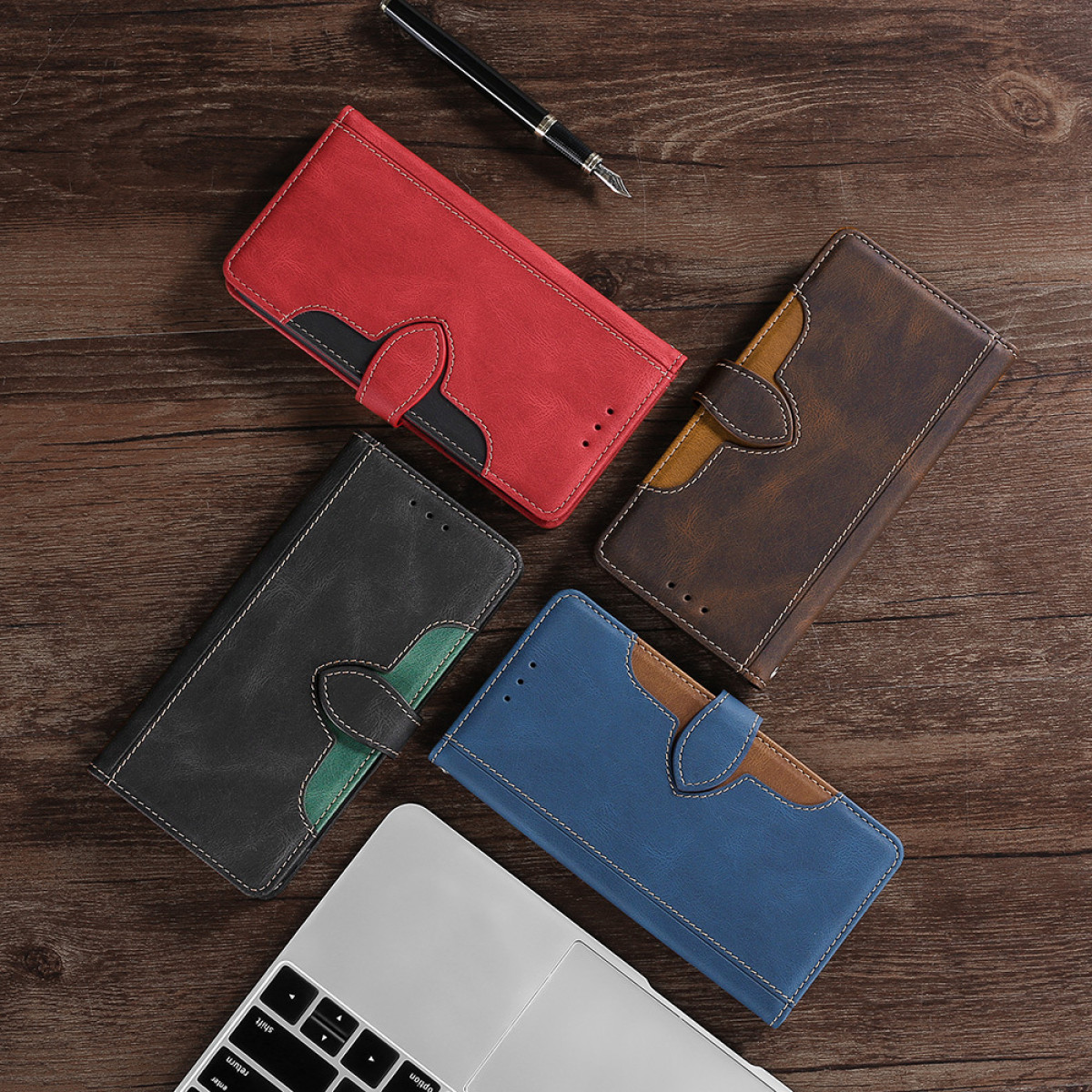 Quattro custodie per telefono in pelle rossa, marrone, nera e blu su legno, con laptop e penna.