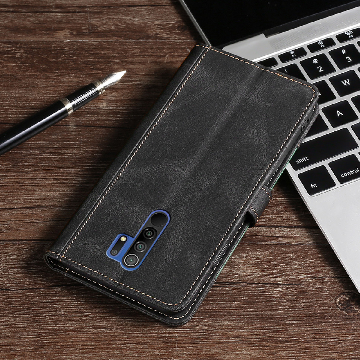 Custodia per telefono in pelle nera aperta su una superficie di legno, con penna e laptop sullo sfondo.