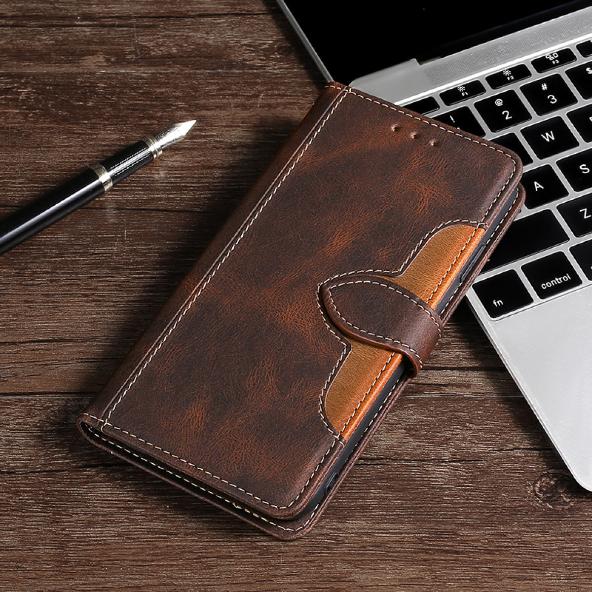 Una custodia per telefono in pelle marrone è appoggiata su un tavolo di legno accanto a un laptop e una penna.