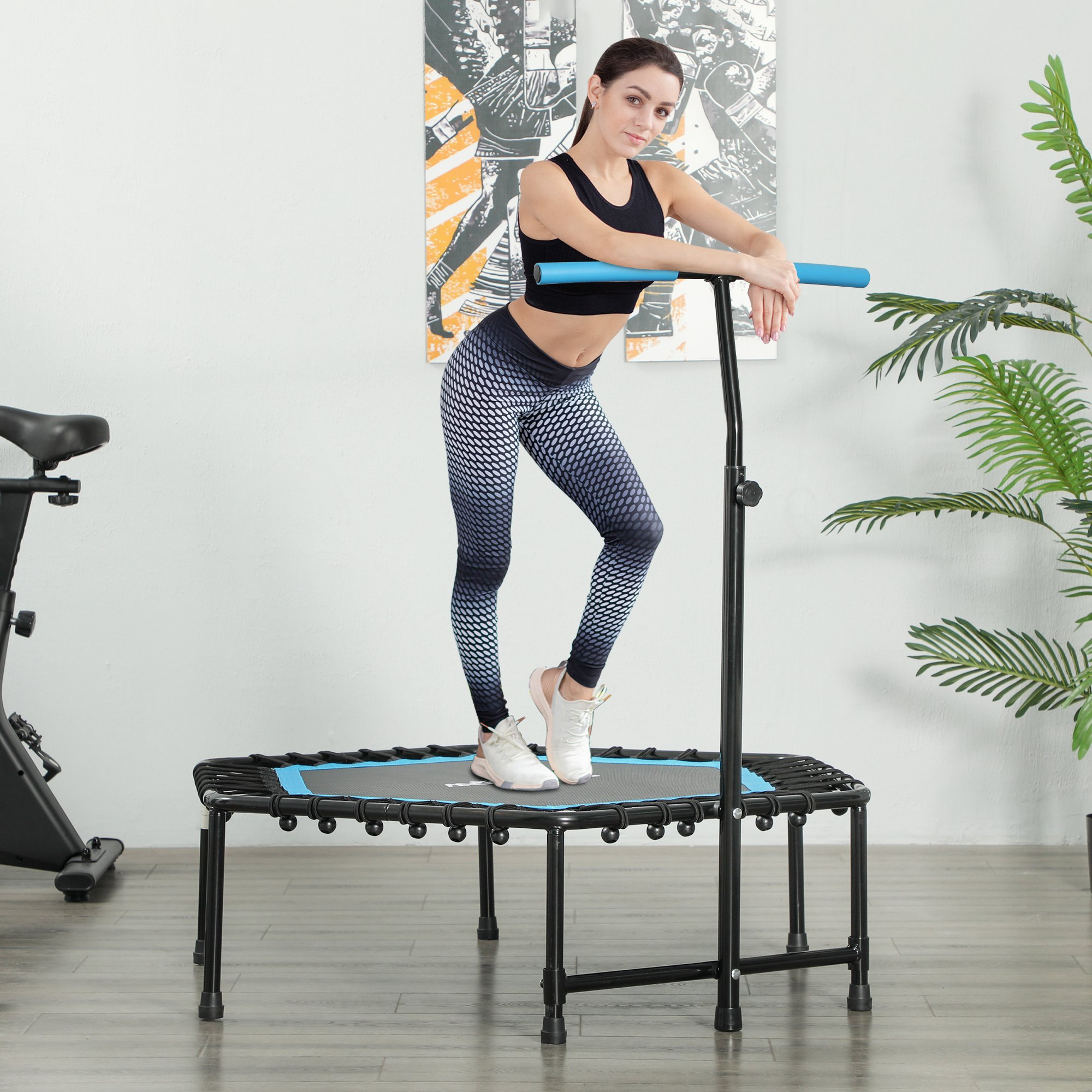 Mujer ejercitándose en un trampolín, con asa de apoyo y pesas.