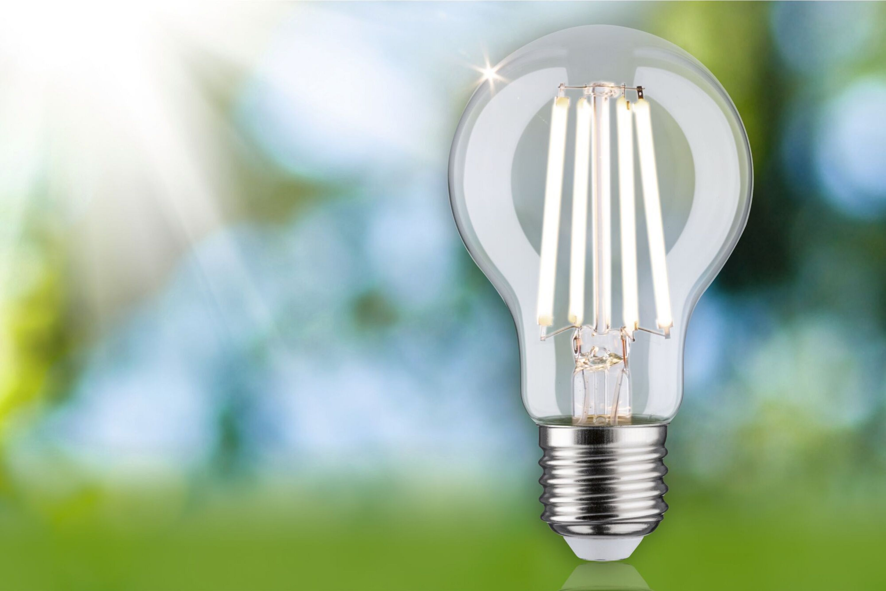 Eine leuchtende LED-Glühbirne mit grünem Hintergrund. Sonnenstrahlen scheinen von links oben herunter.