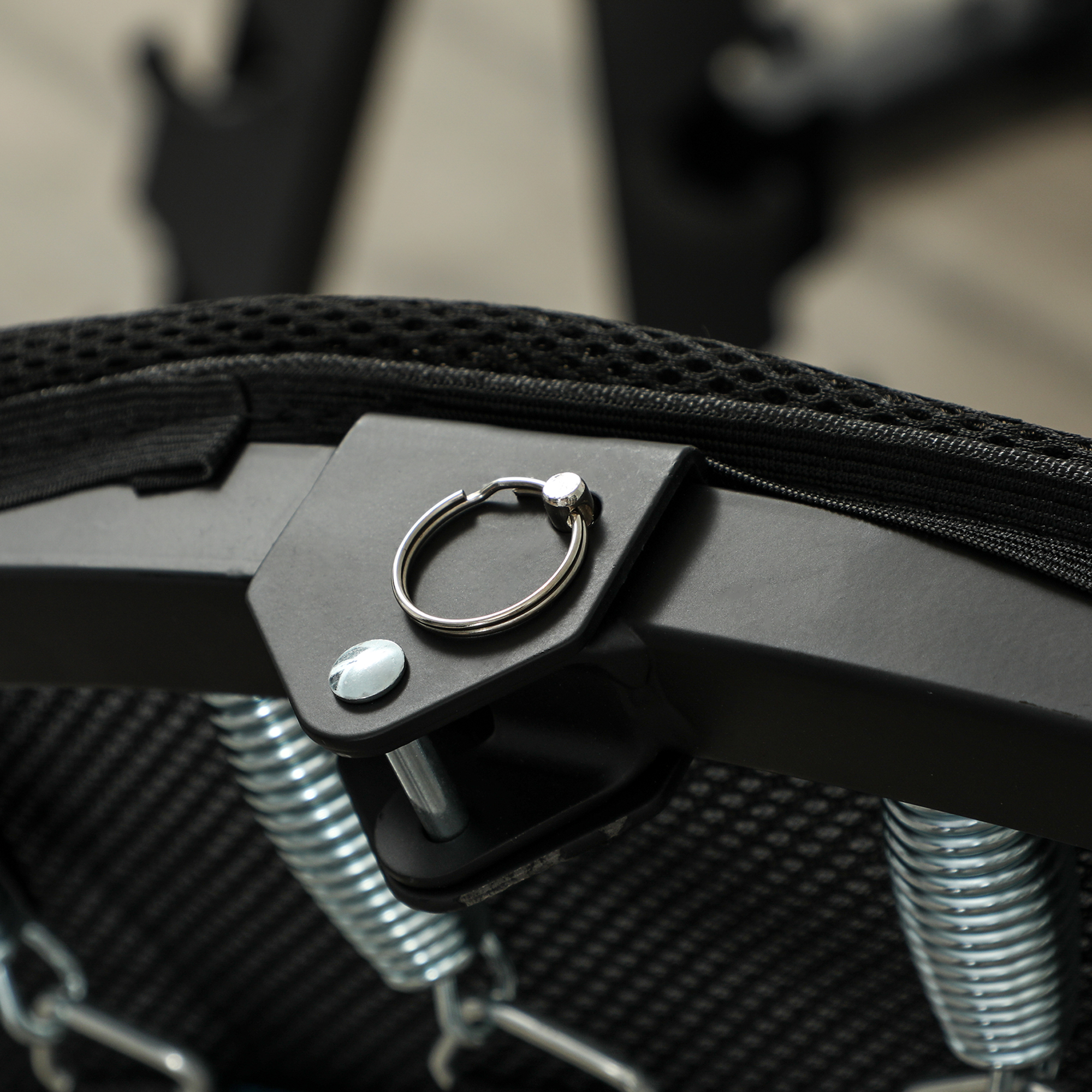 Primer plano de un trampolín negro con resortes metálicos y un accesorio de anillo para un asa.
