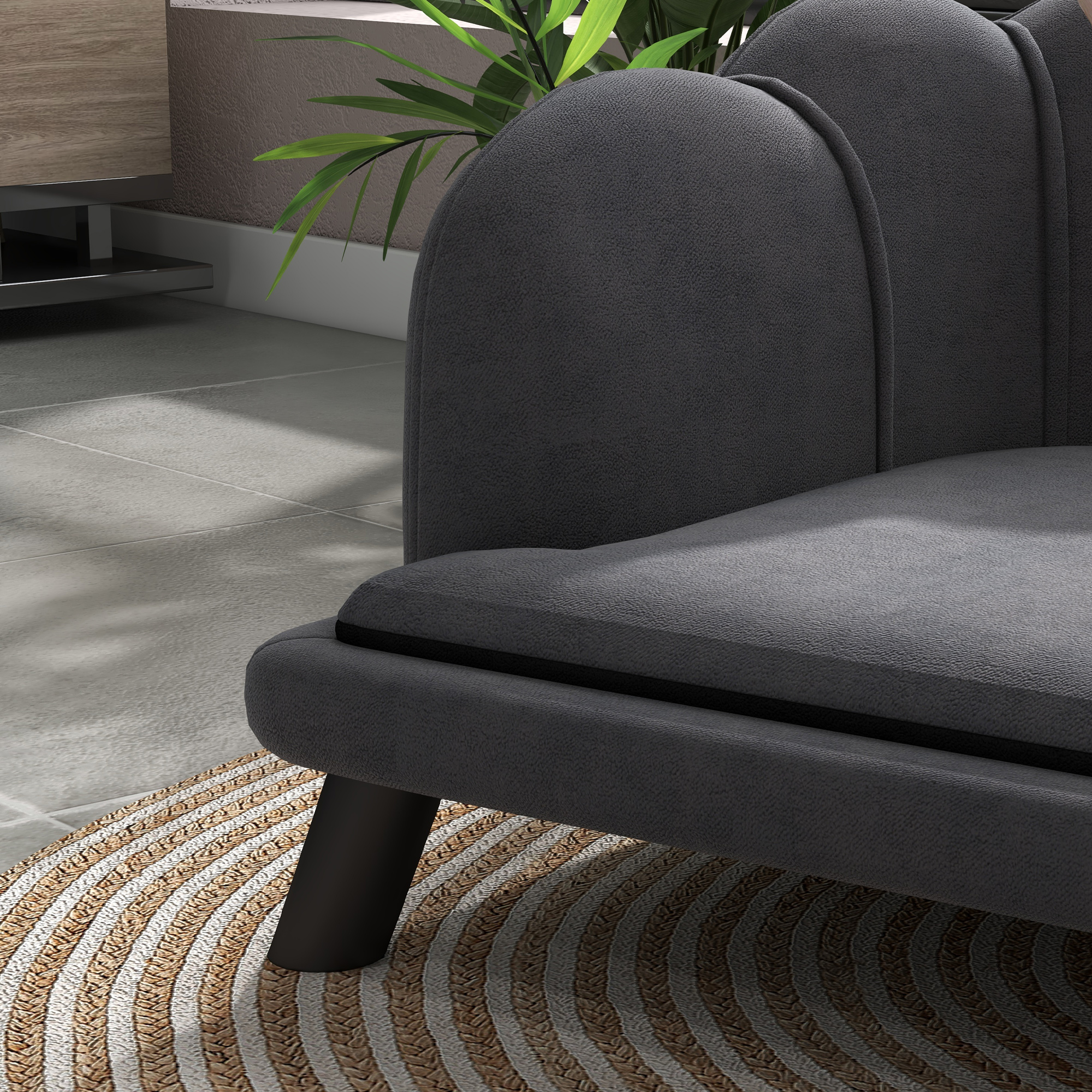Nahaufnahme eines grauen Sofas mit schwarzen Beinen, das auf einem runden Teppich mit Webmuster steht.